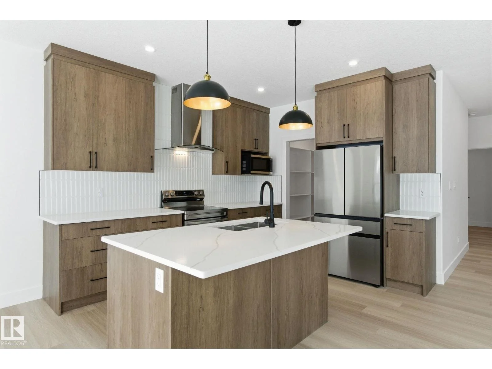 Modern kitchen featuring wooden cabinets, a white marble island with a black faucet, stainless steel appliances, and black pendant lights.