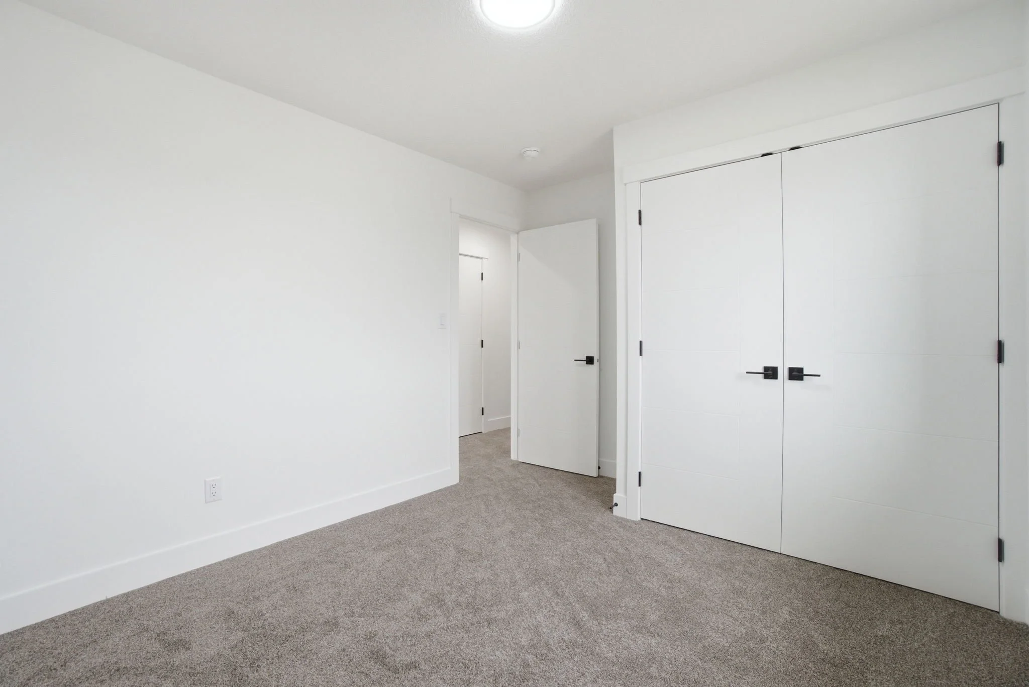 Empty room with white walls, beige carpet, closet with double doors, and open doorway.