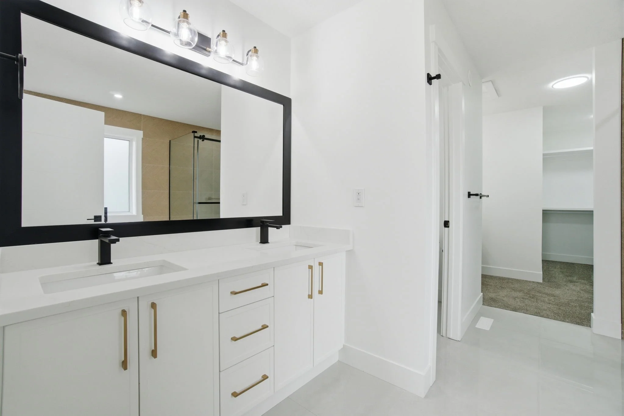 Modern bathroom with white vanity, large mirror, black fixtures, and walk-in shower with glass enclosure.