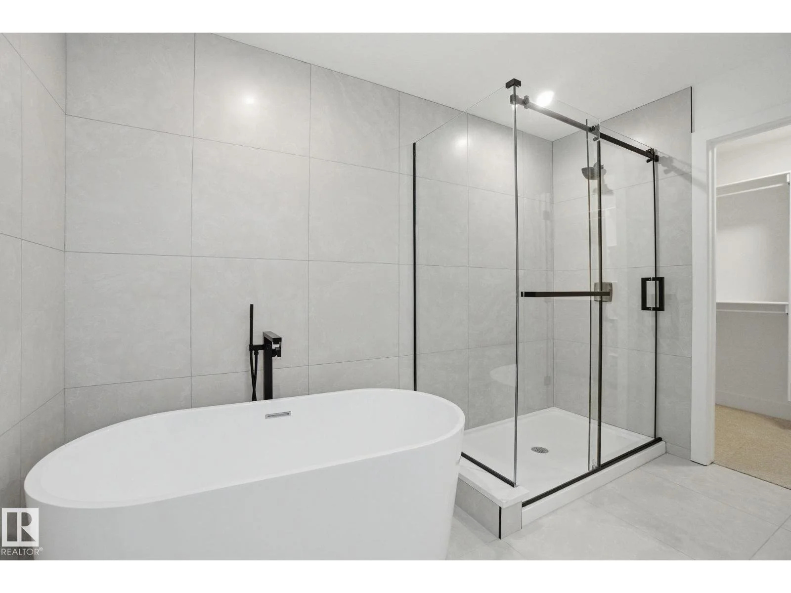 Modern bathroom featuring a freestanding bathtub and a glass-enclosed walk-in shower with black hardware, minimalistic design, gray tiled walls, and an open closet space.