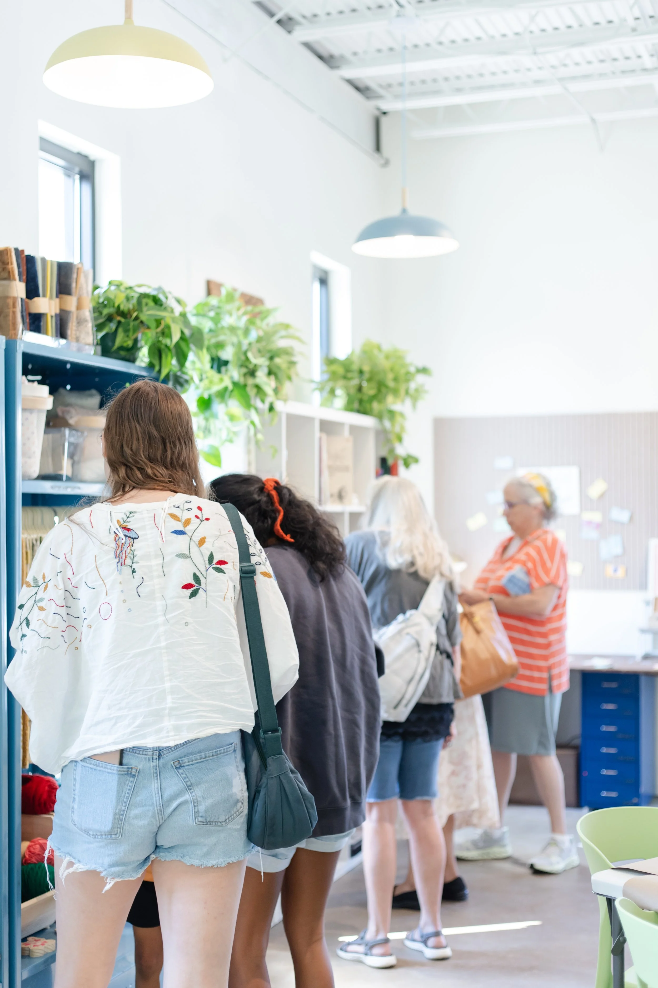 Angled shot of The Craft Room merchandise walls with happy shoppers and colorful pendant lights. 