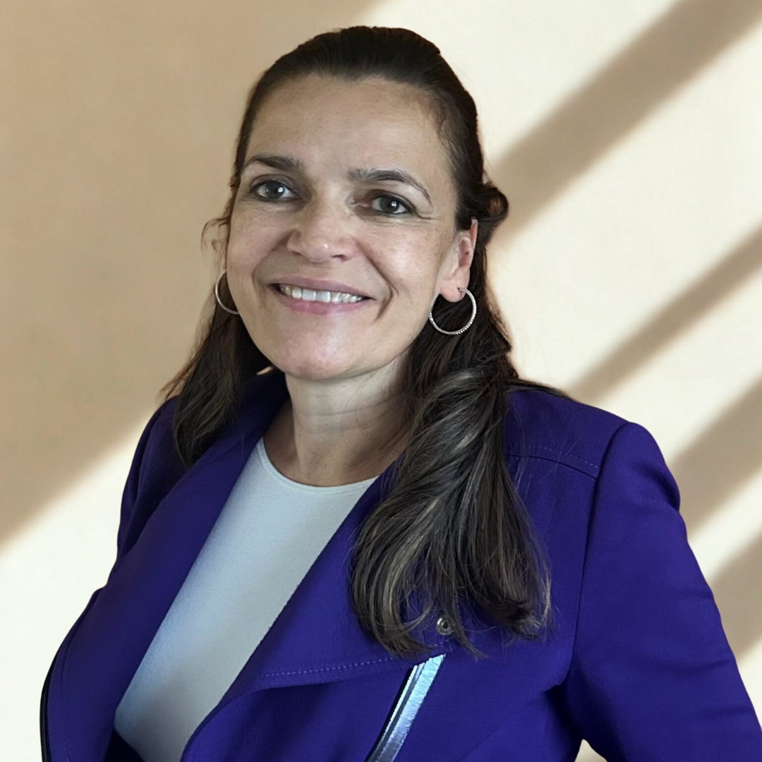 A woman with long brown hair, wearing hoop earrings and a purple jacket, smiling at the camera.