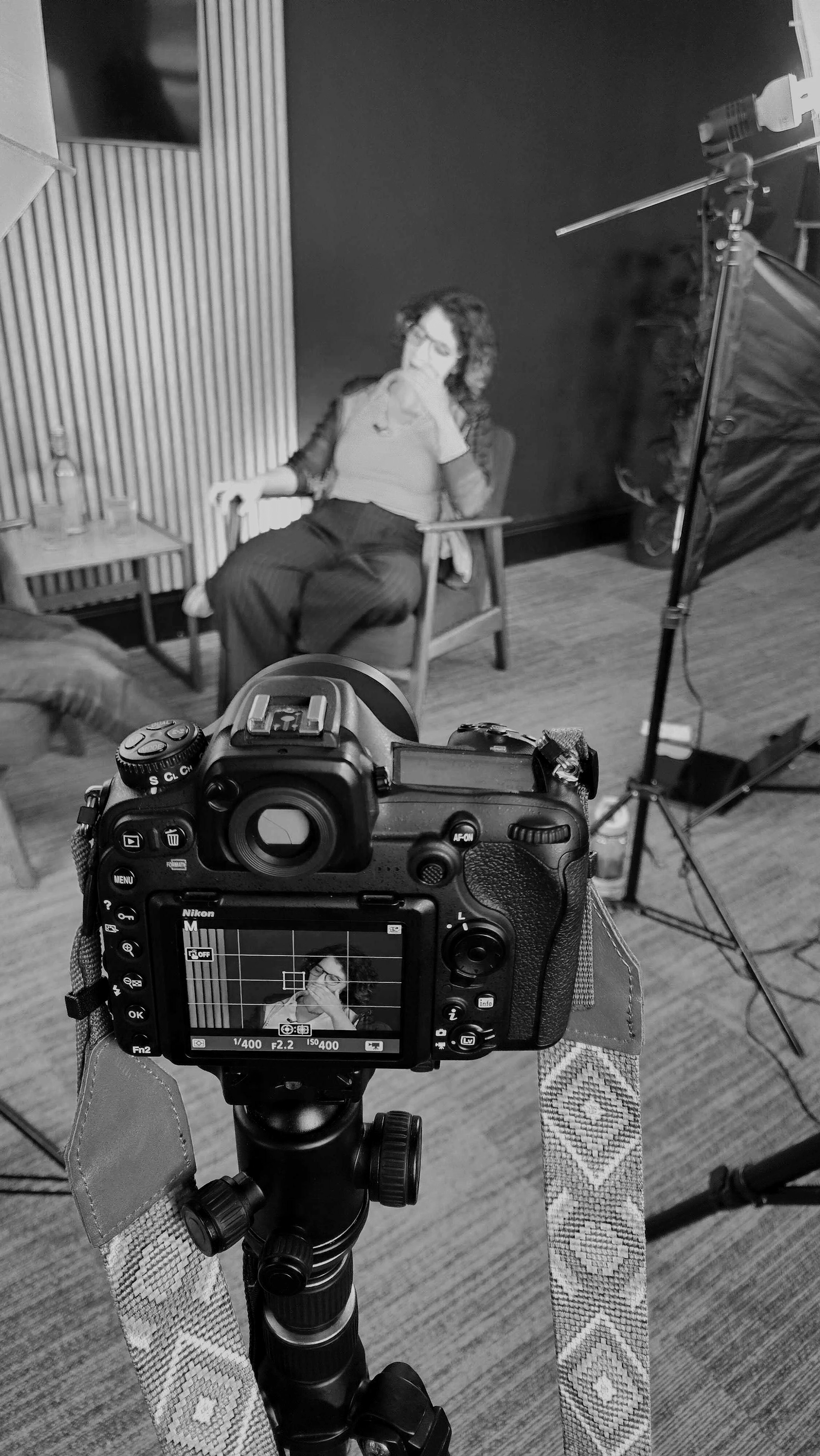 A professional production shoot setup capturing Aoife Buggy during Podcast production, sitting in a chair, with video equipment including a camera on tripod, studio lights, and a backdrop in the background.
