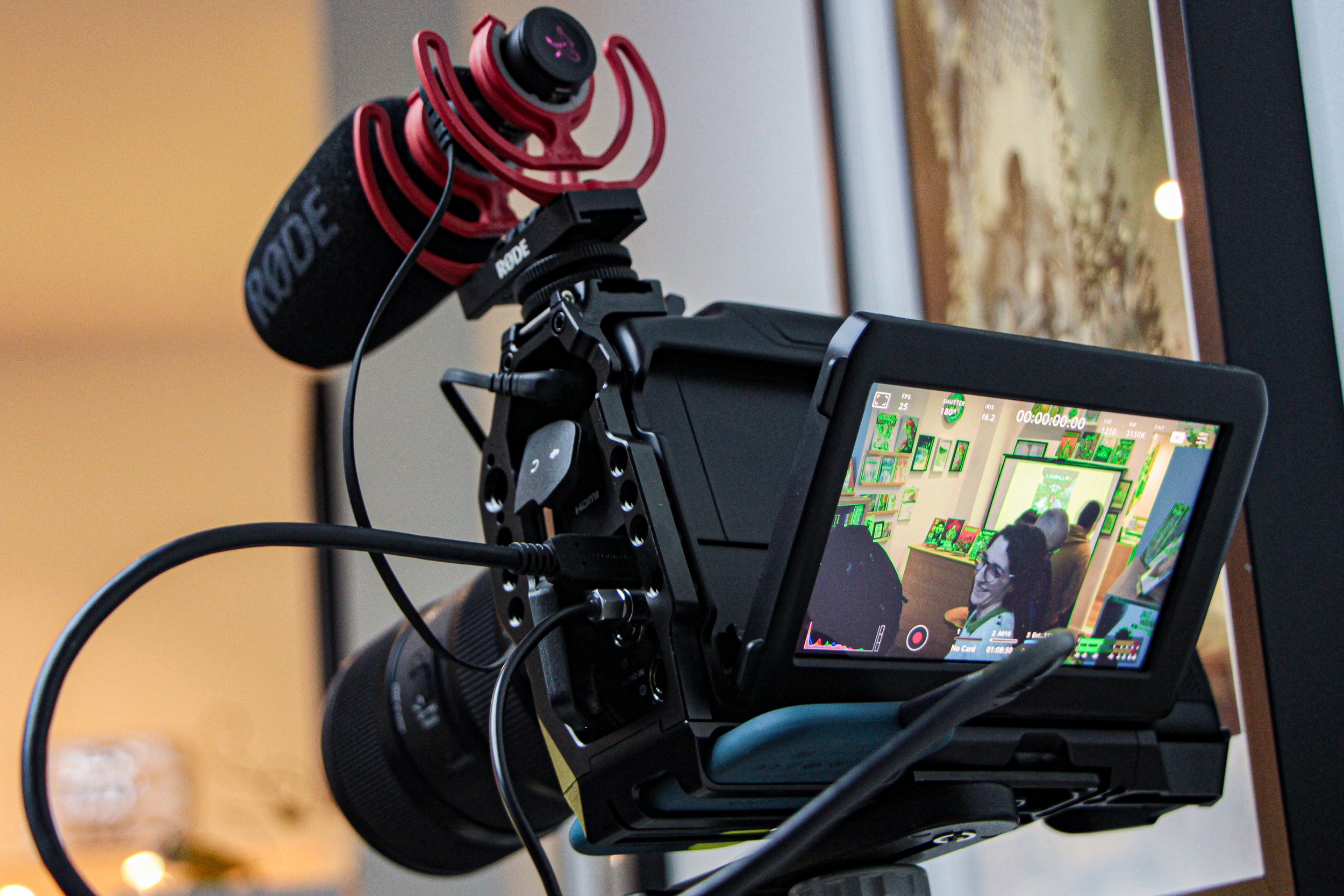 Documentary-style picture of an on-location production shoot recording footage with Aoife Buggy in frame on the camera display. Close-up of a professional video camera setup with a mounted microphone, for podcast recording.
