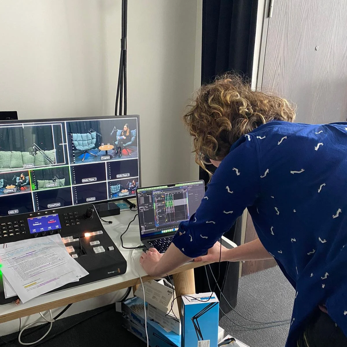 Aoife Buggy is running a podcast production with a multi-camera setup. Working on video editing or live production setup on a desk with multiple monitors, papers, and recording equipment.