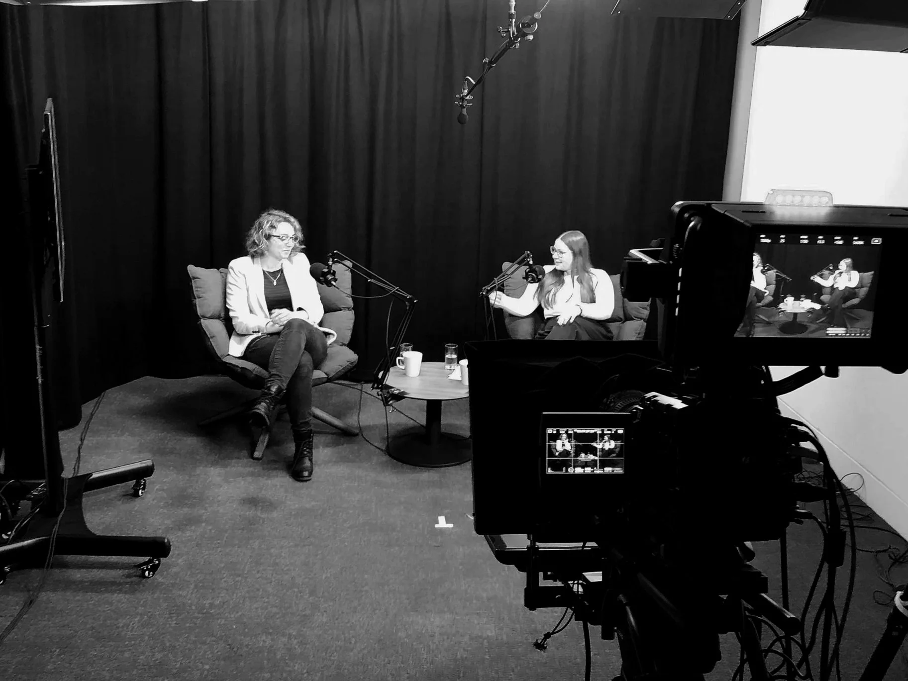 Aoife Buggy, freelance video editor and motion graphic design , is engaged in a podcast interview or conversation in a recording studio with black curtains, microphones, and a camera capturing the scene.