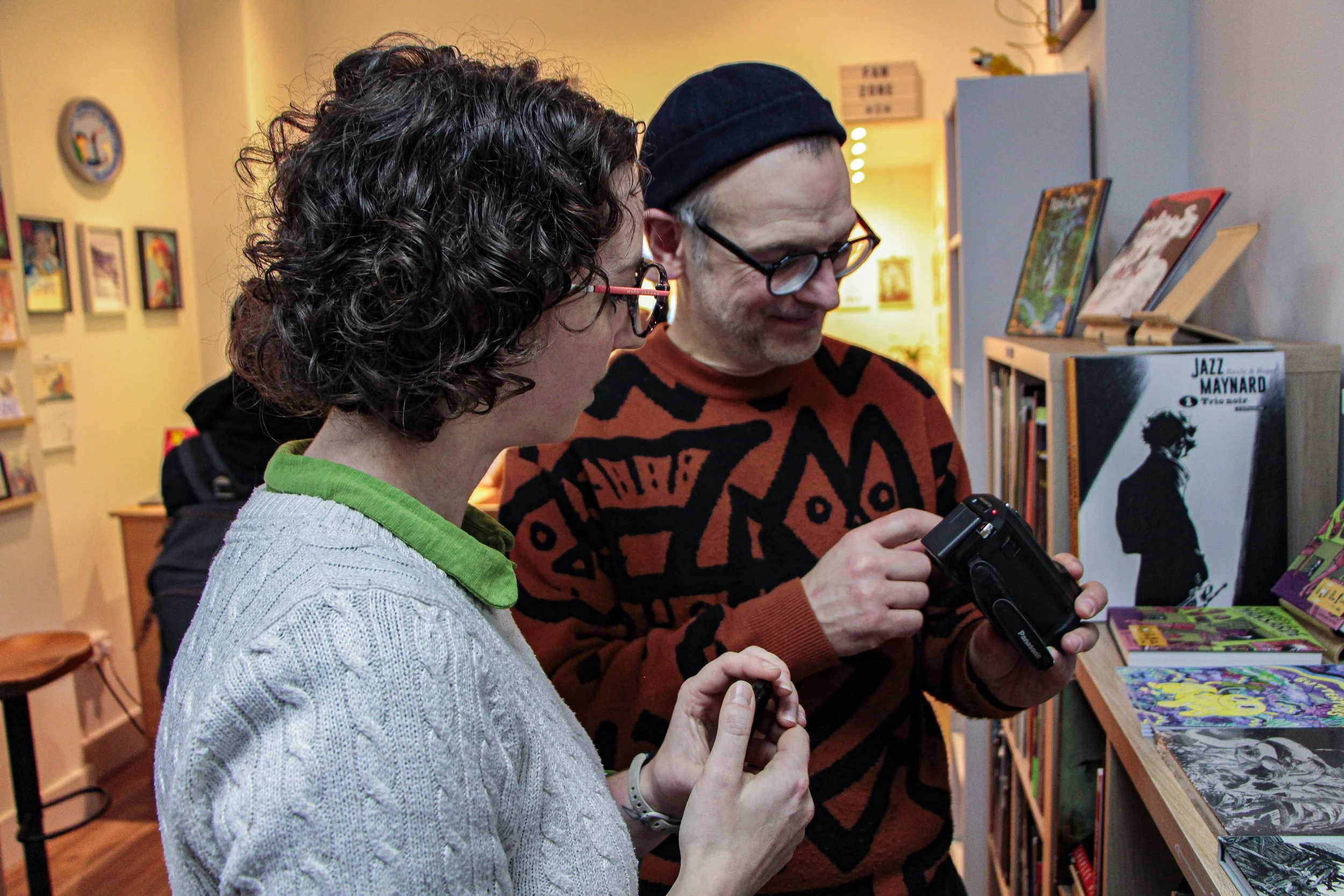 Aoife Buggy, freelance video and motion graphics, is interacting with a client during a podcast recording in Edinburgh, Scotland. On location shoot with camera lights and sounds in a local bookshop with artwork on the wall behind them.