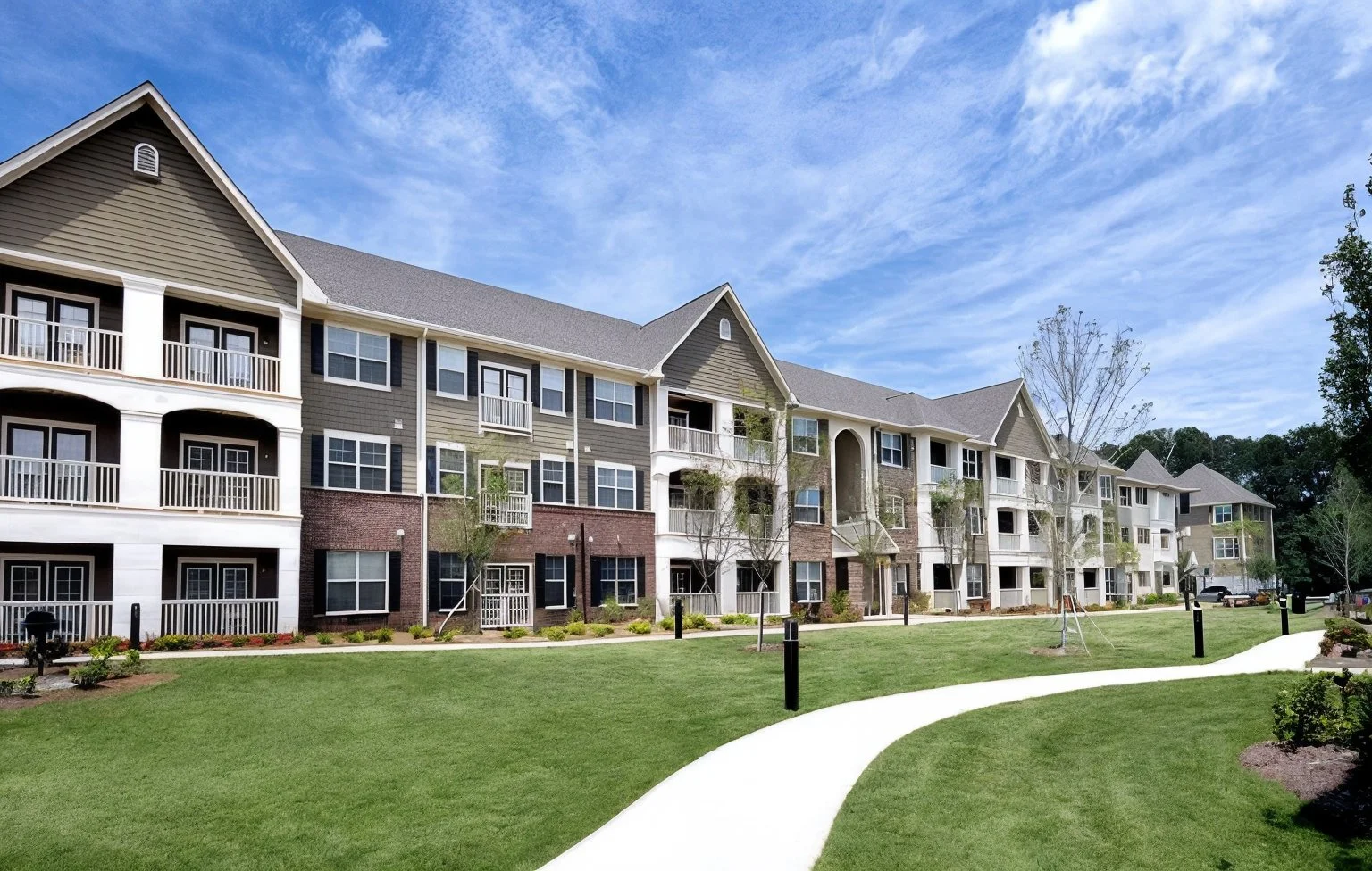 A path winds in front of multifamily apartment buildings with grass on either side.