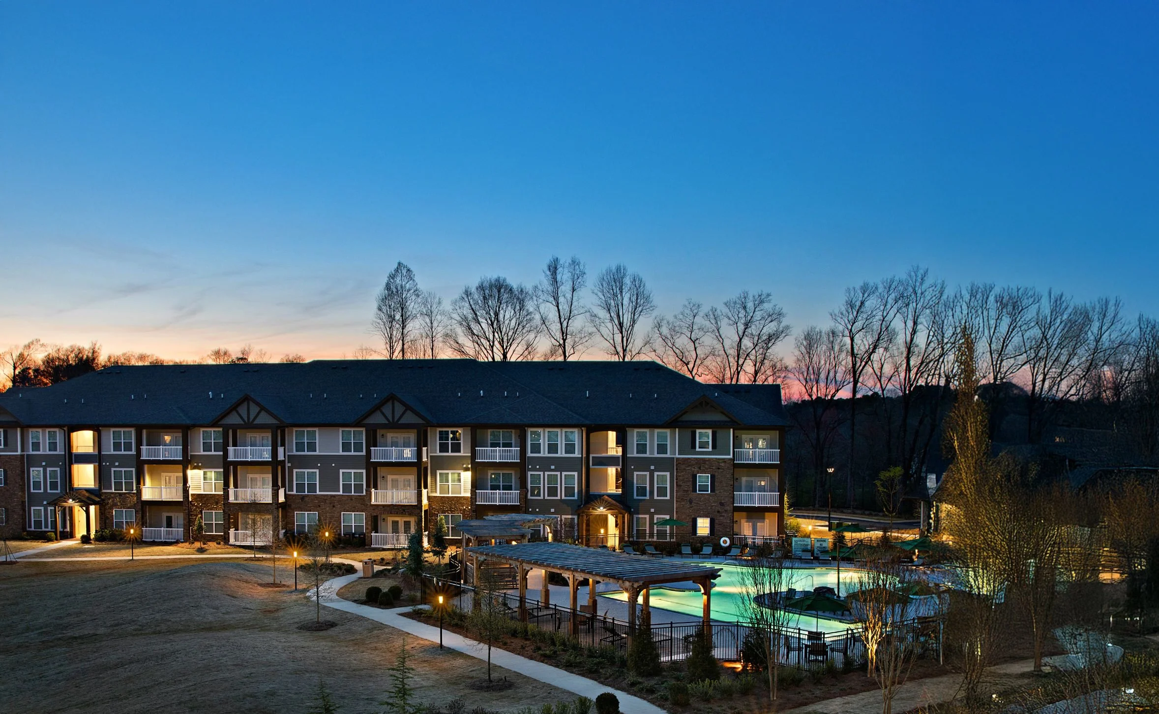 Multifamily apartments at dusk with a pool in front of them.