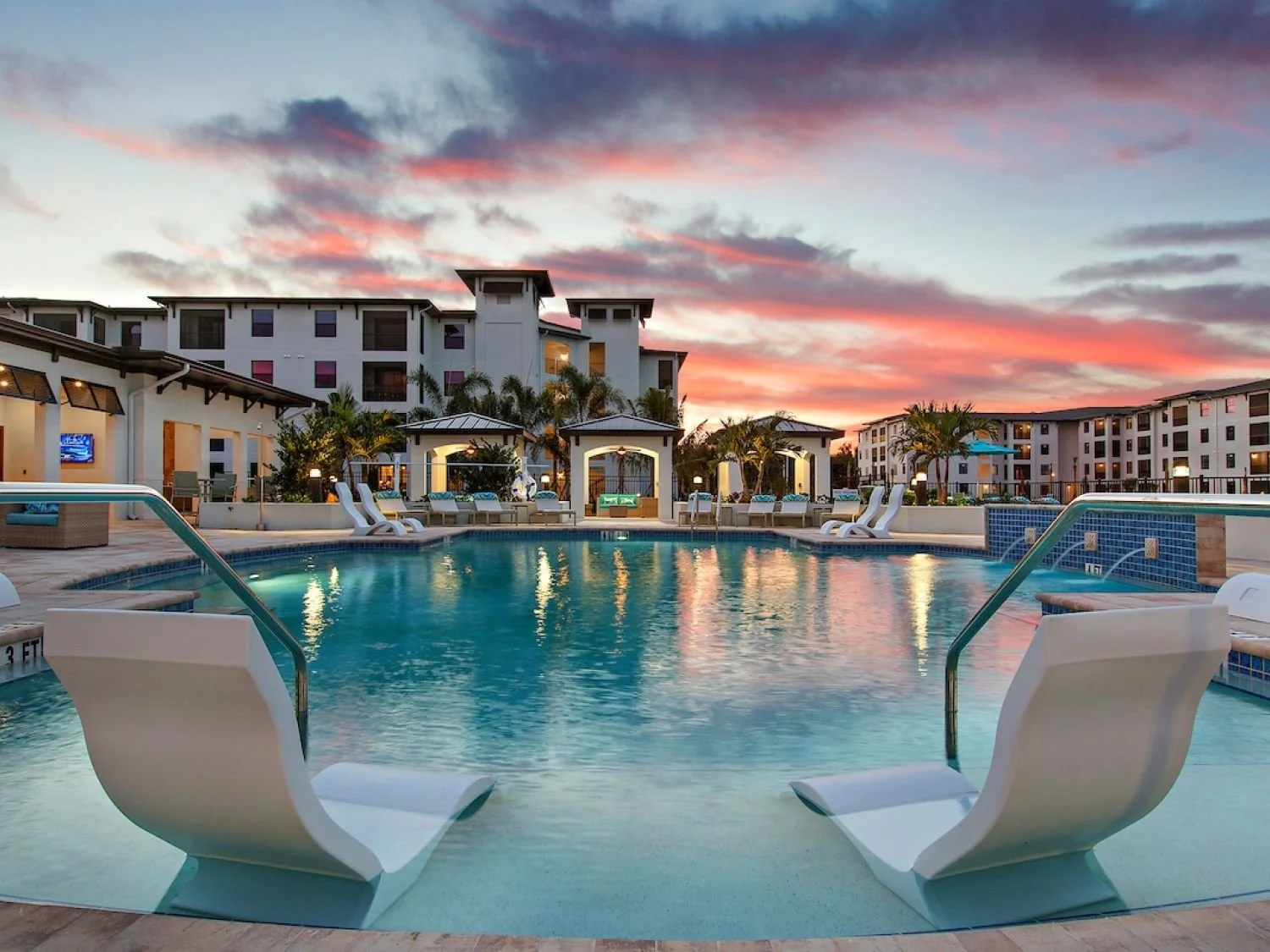 Two lounge chairs sit in a pool, looking out at a high-end multifamily apartment building