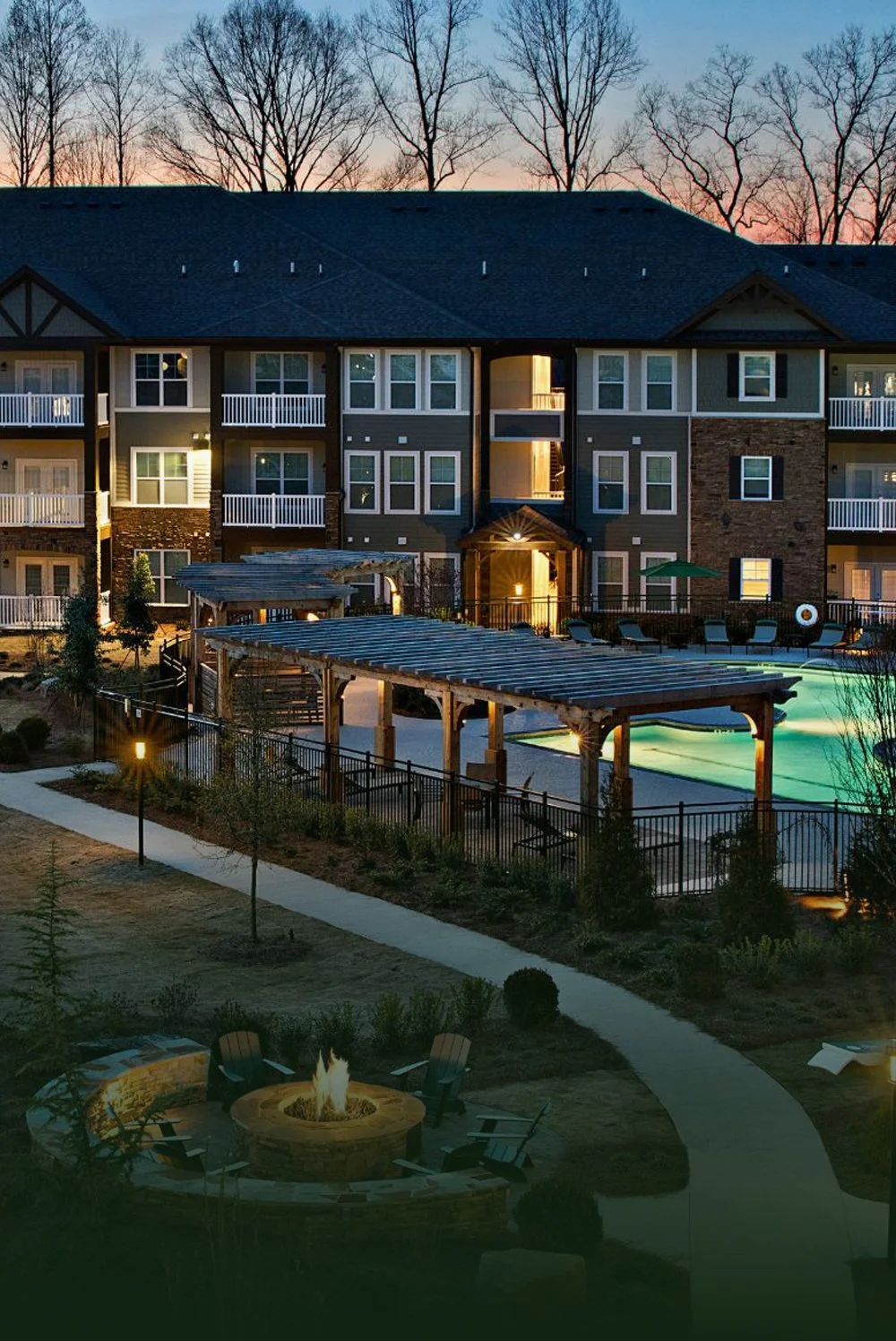 A multifamily apartment building at dusk with a pool situated in front of it.