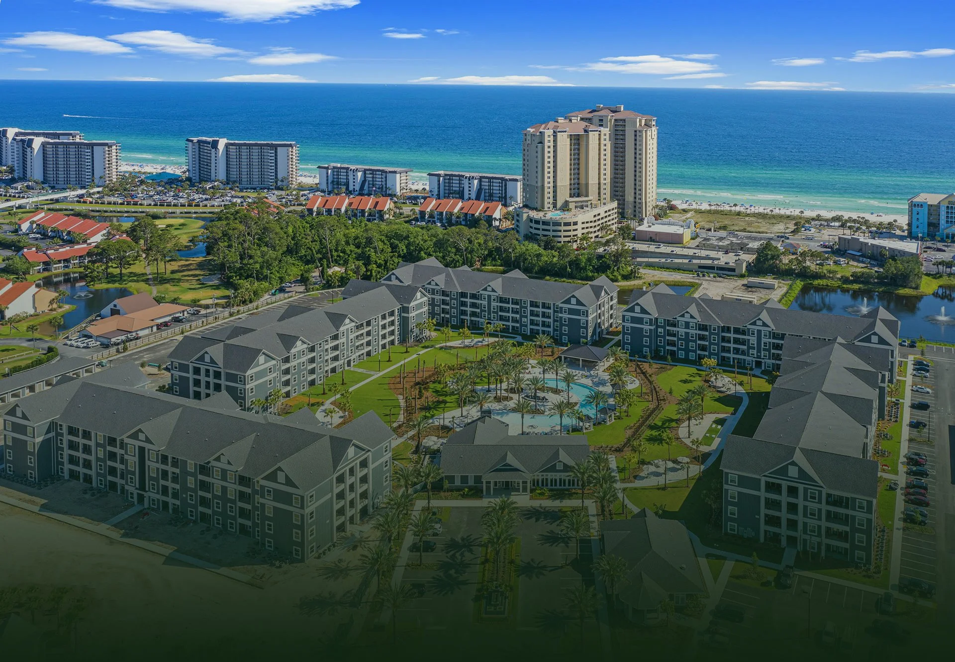 Multifamily apartment buildings surround a pool with the beach in the distance.