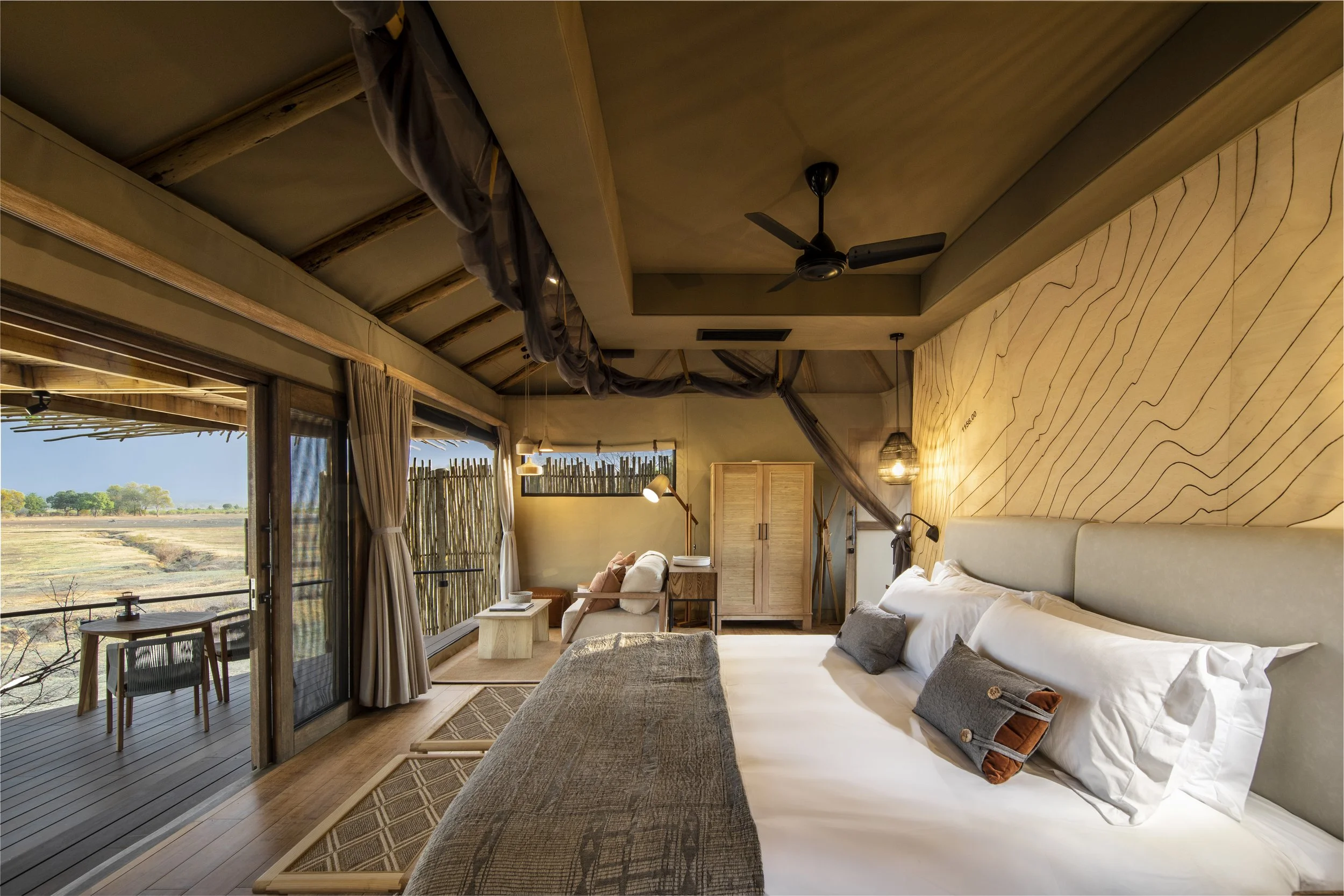 Interior of a cozy bedroom with a large bed, window view of nature, wooden furniture, and decorative lighting.