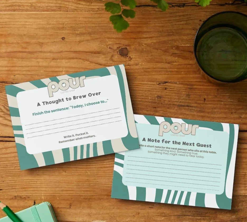 Branded cafe cards on table inviting guests to leave notes or reflections for others, fostering offline connection and thoughtful customer moments.