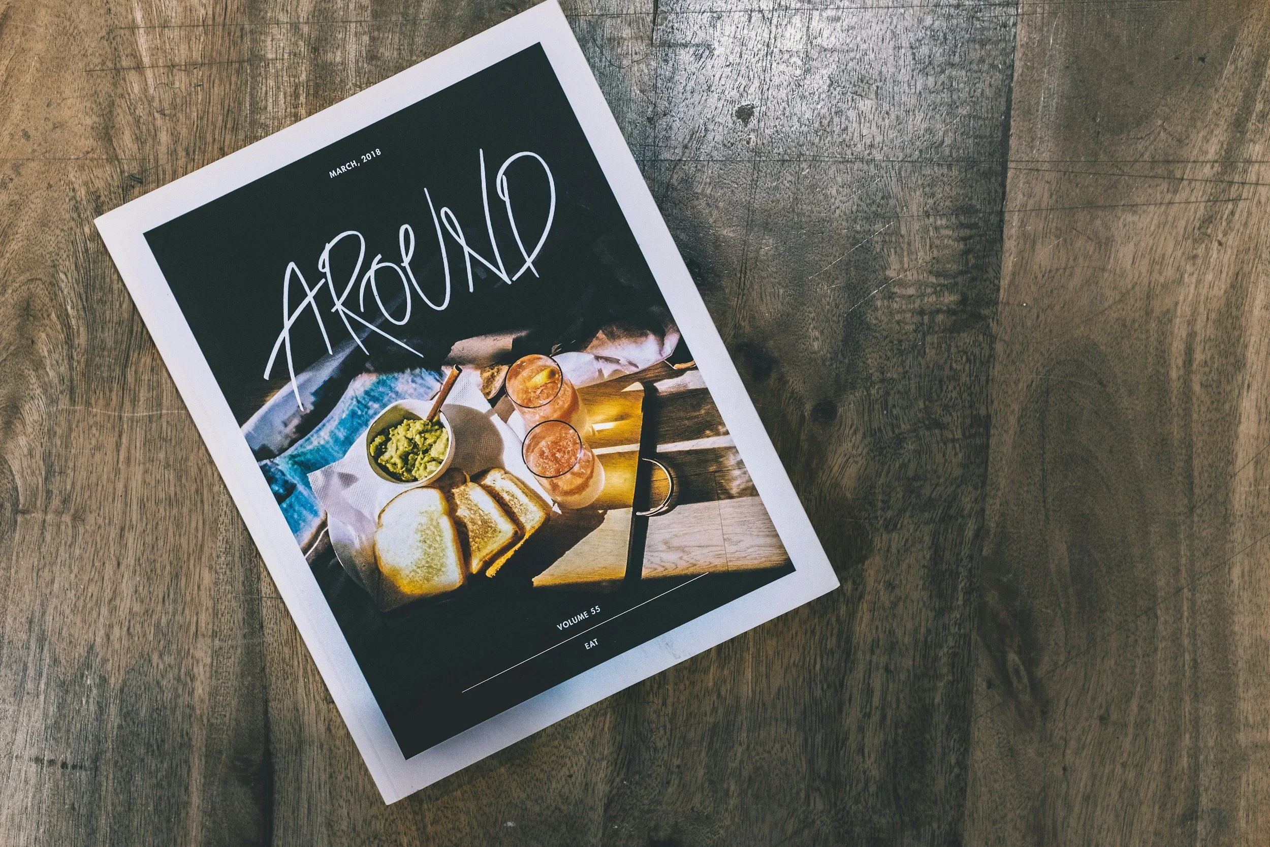 Printed magazine titled 'AROUND' with a styled food scene on a rustic timber table, reflecting tangible, community-focused storytelling design.