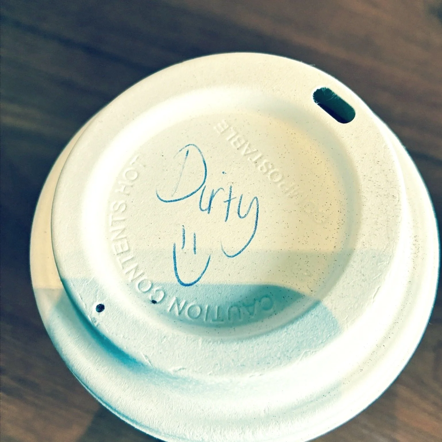 Coffee cup lid with handwritten 'Dirty :)' doodle, symbolising small, memorable offline brand moments that spark joy and customer connection.
