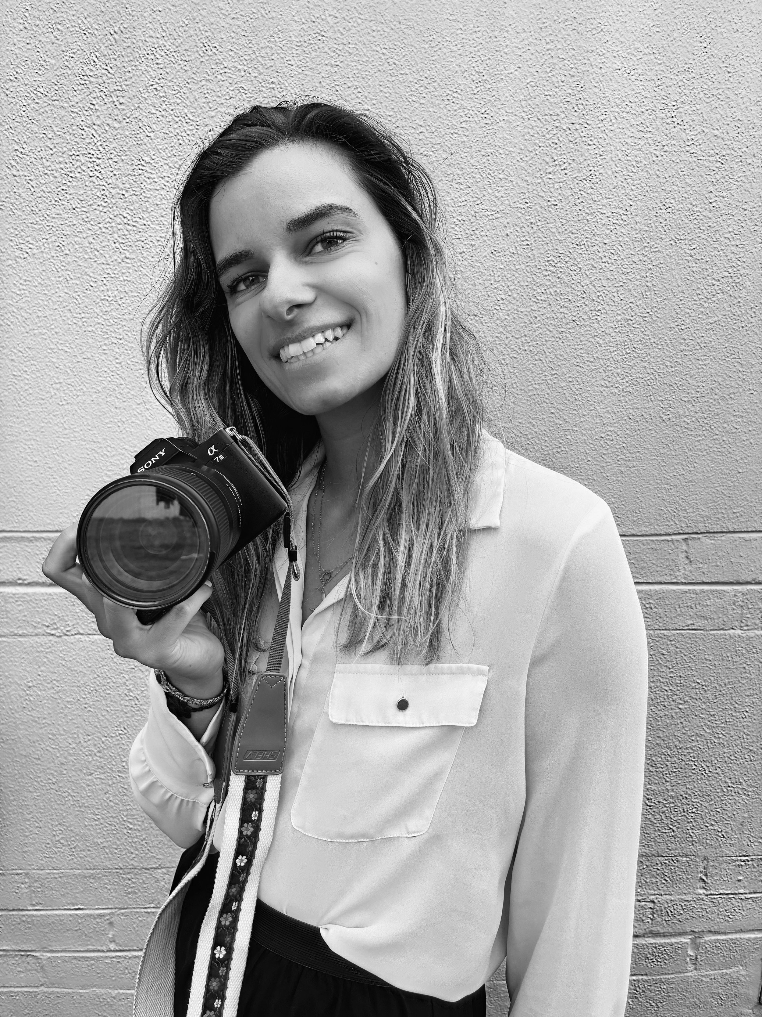 Young female photographer smiling while holding a professional camera. Capturing the human side of brand storytelling and visual content creation.