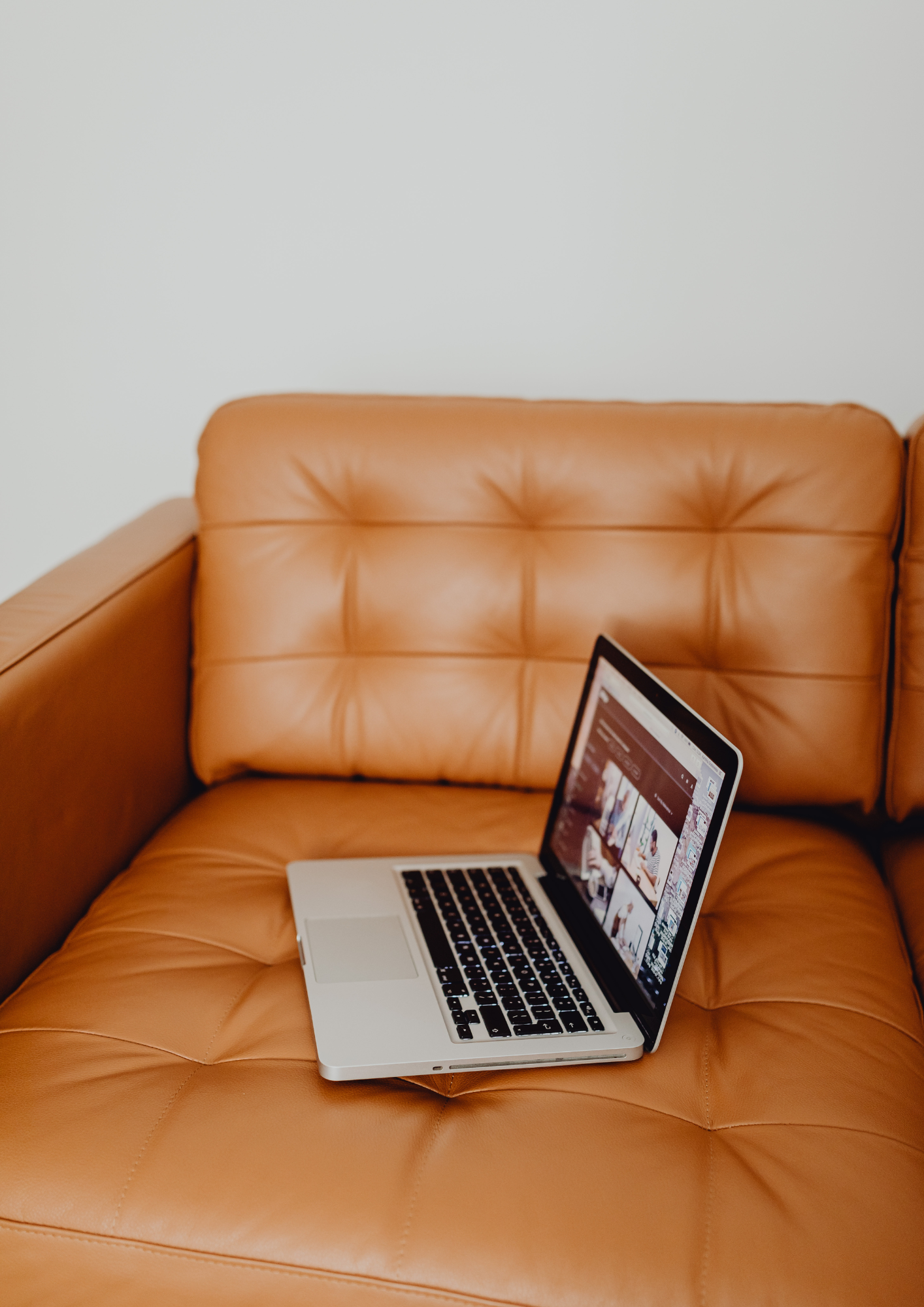 Open laptop resting casually on a caramel leather sofa, symbolising relaxed, founder-led branding workspaces and digital freedom.