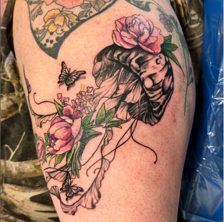 Tattoo of a jellyfish intertwined with pink flowers and two butterflies on the upper arm by Willow Thomason located in Wolfville, Nova Scotia.