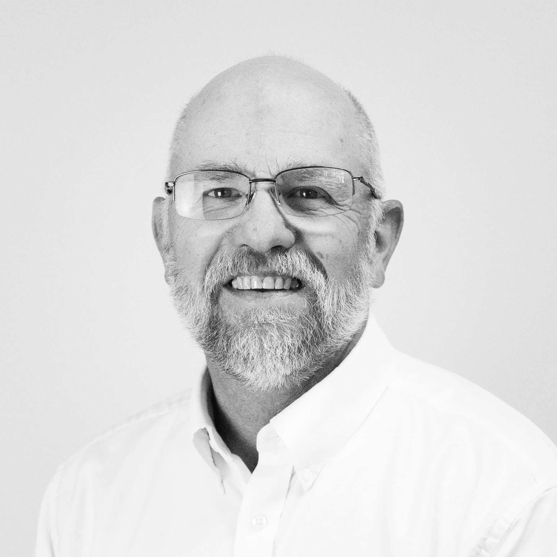 Black and white portrait of a smiling middle-aged man with glasses, a beard, and short hair, wearing a white collared shirt.