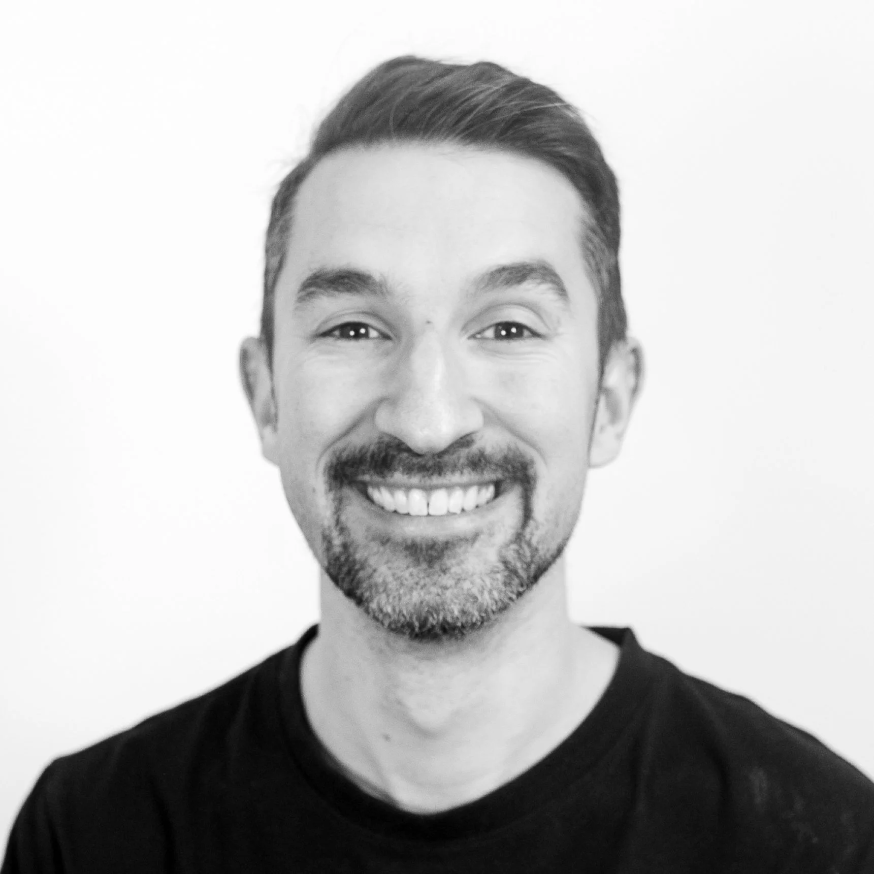 Black and white portrait of an older man smiling, resting his chin on his hand, wearing a dark polo shirt.
