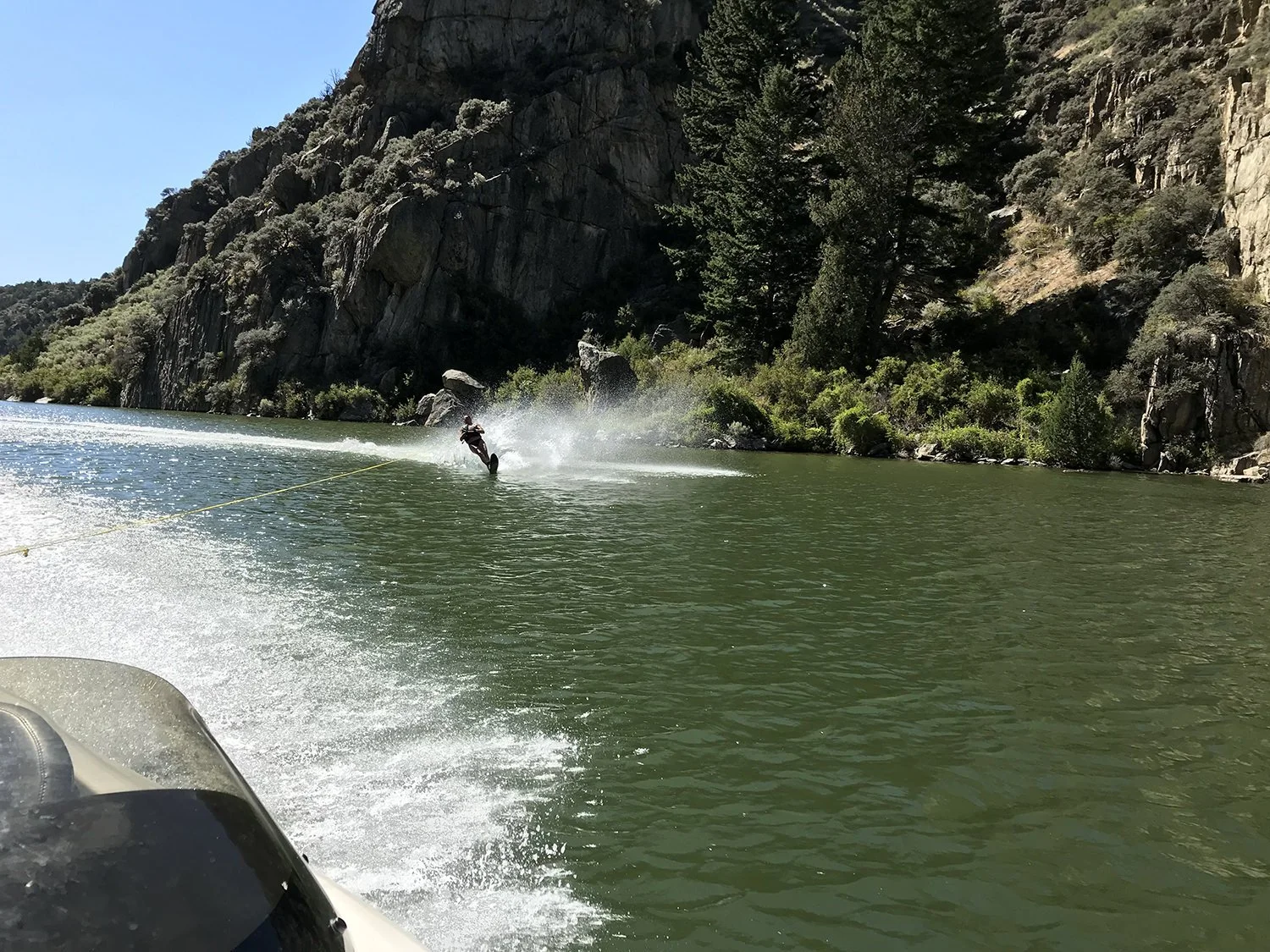 Person water skiing on a river with cliffs and trees in the background.