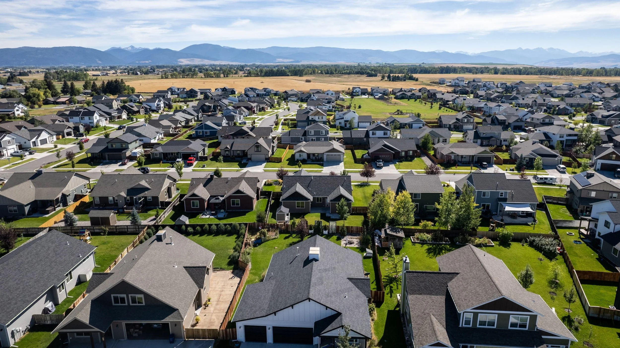 Aerial view of a residential neighborhood with houses, yards, and streets, with mountains in the background.