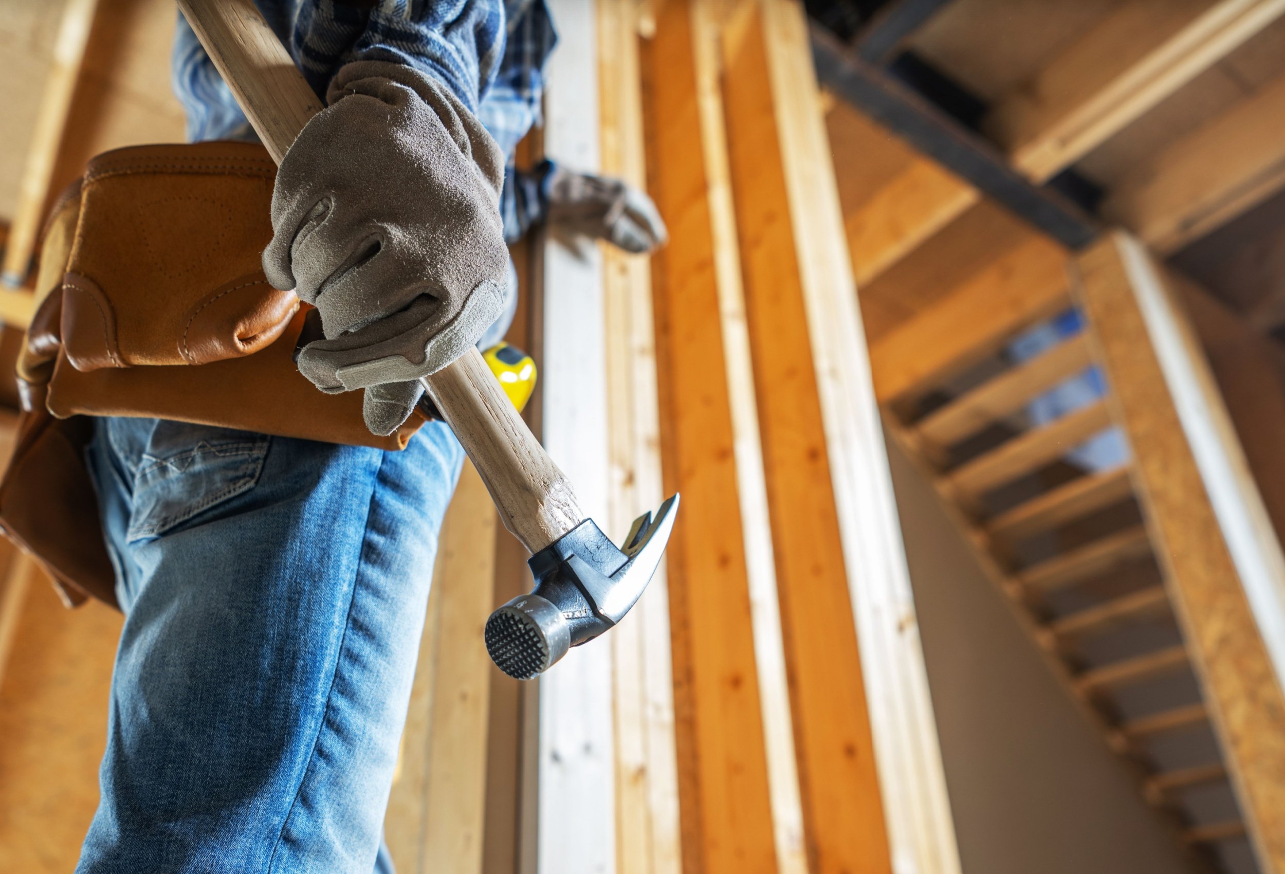 A person wearing gloves holding a hammer inside a wooden construction frame.