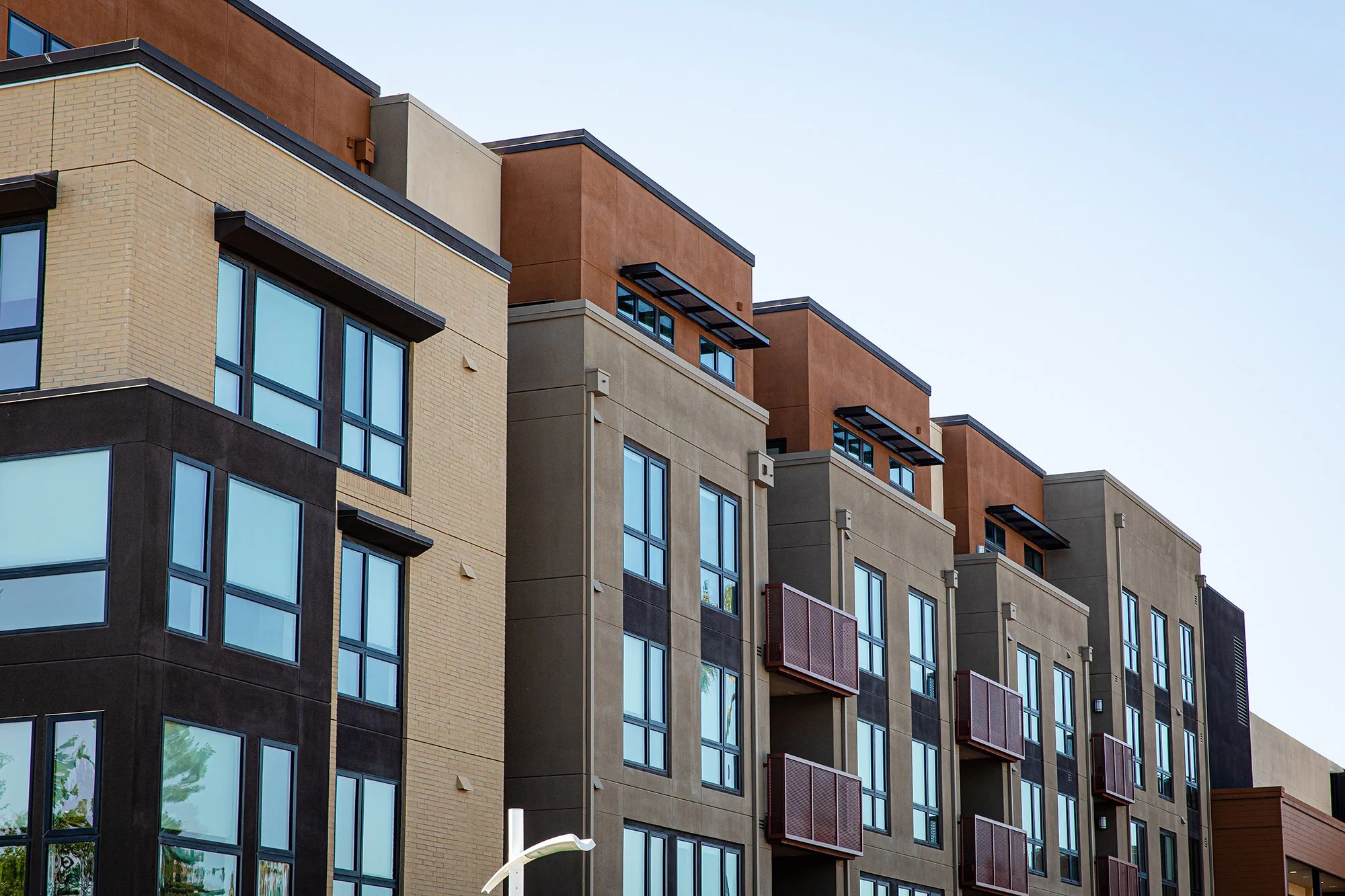 Modern apartment building with large windows and colorful facade panels against a clear blue sky.