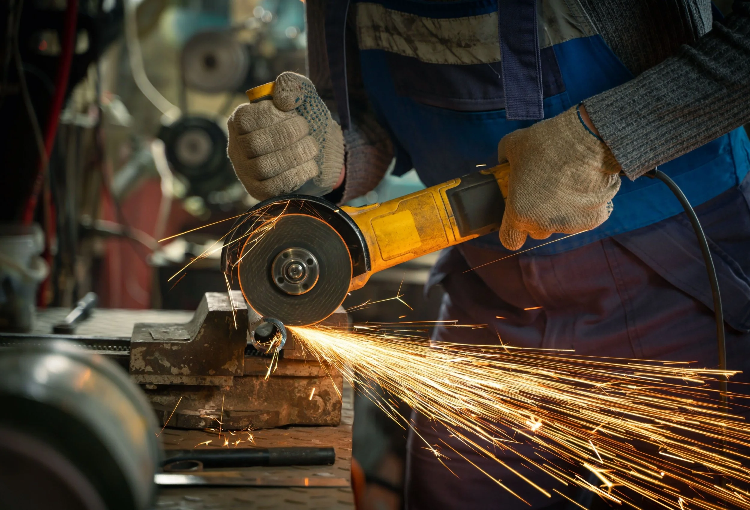 A person wearing gloves and safety clothing using an angle grinder, cutting metal with sparks flying.