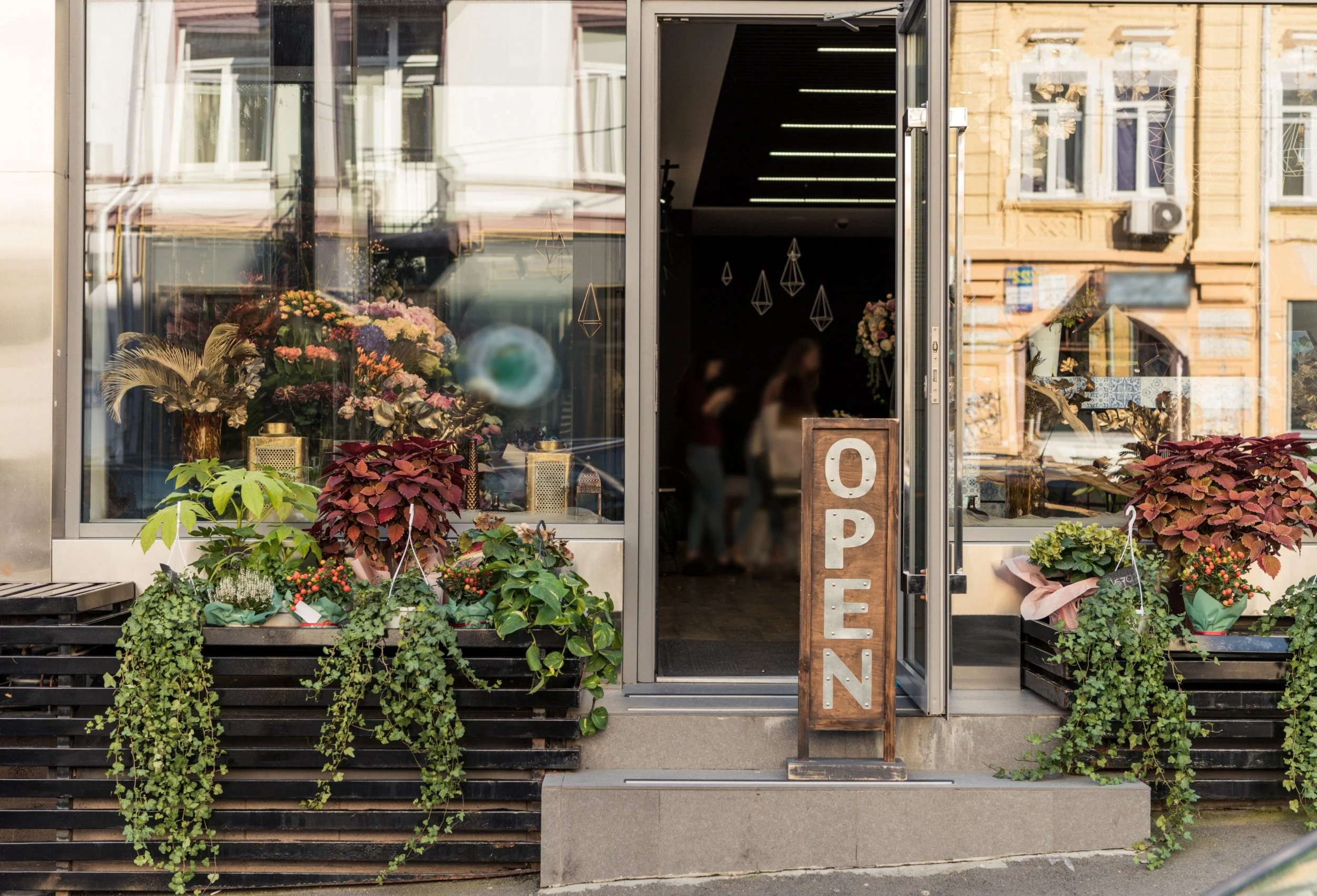 Flower shop with large glass windows displaying various flowers and plants outside, and a wooden 'Open' sign on the door.