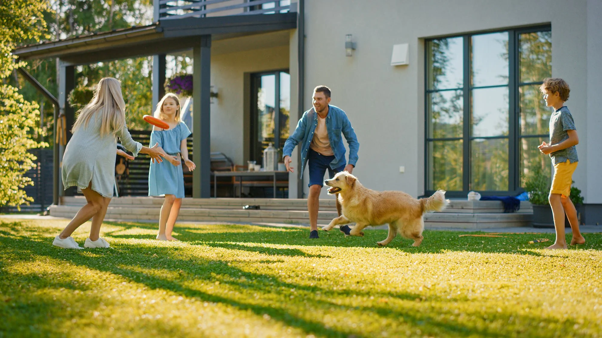 A family playing with their dog outside on the lawn of a modern house on a sunny day.
