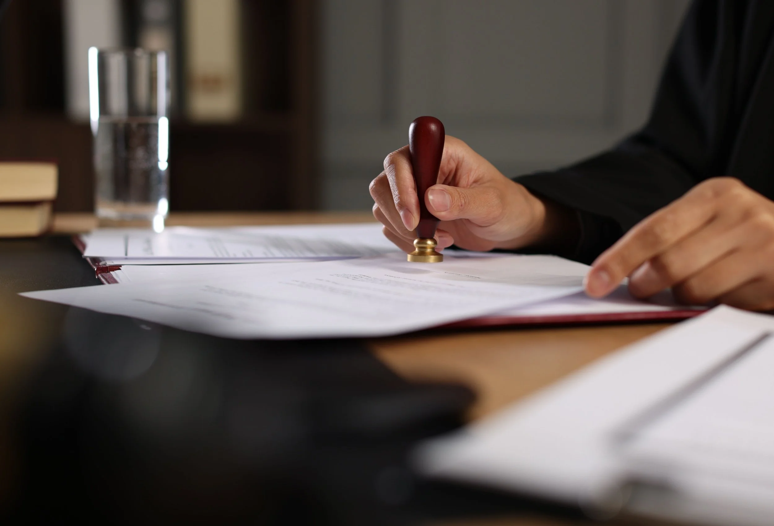 Close-up of a hand using a wax seal stamp on a document in an office setting.
