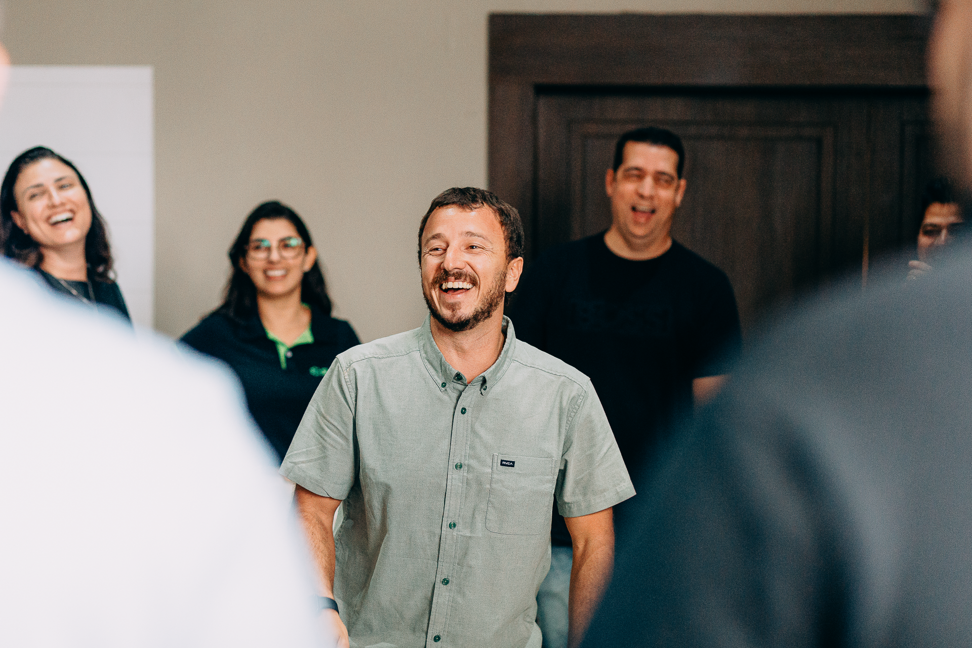 Homem sorridente em reunião com colegas de trabalho, todos rindo e aparentando alegria.