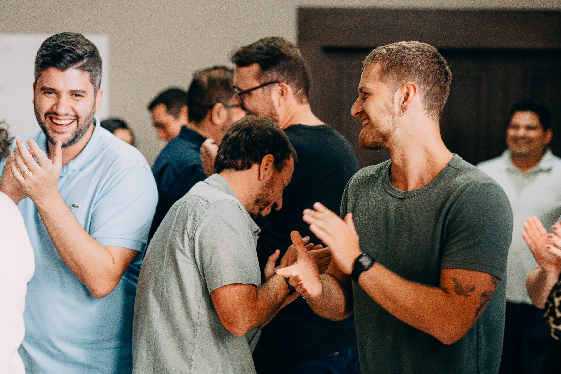 Homens sorridentes em uma reunião ou evento social, interagindo e cumprimentando um ao outro com entusiasmo.