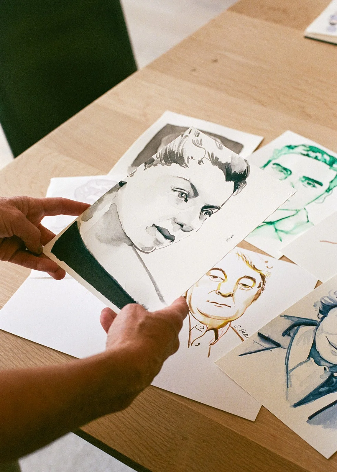 Person holding a black-and-white portrait of a woman, with other colorful portraits on a table.