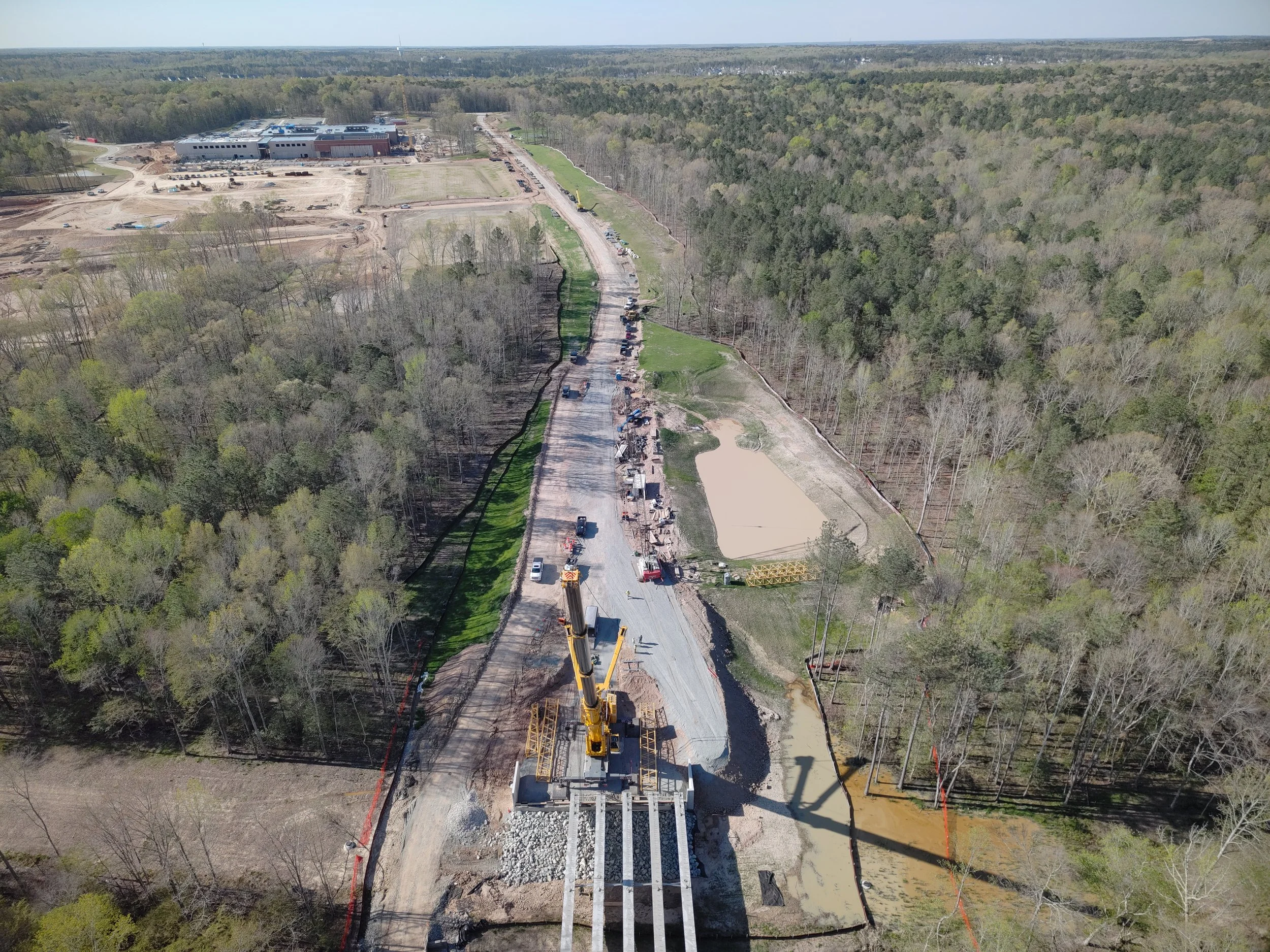 Curb and asphalt installation begins. Bridge work continues with girder erection. Pipe work continues.