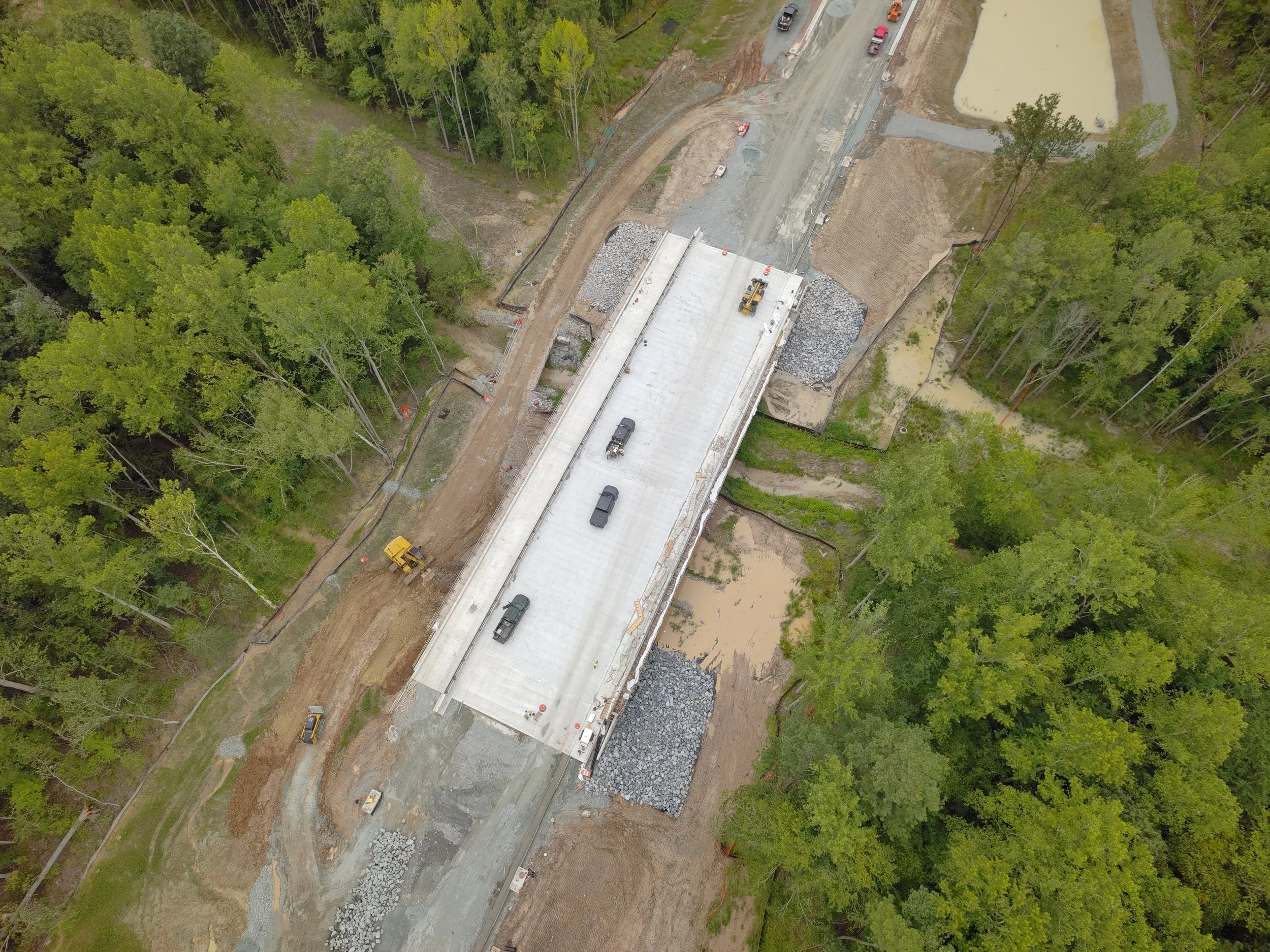 Roadway work continues with curb/underdrain installation and paving to follow. Work on the bridge reaches final stages with sidewalk and railing installation.