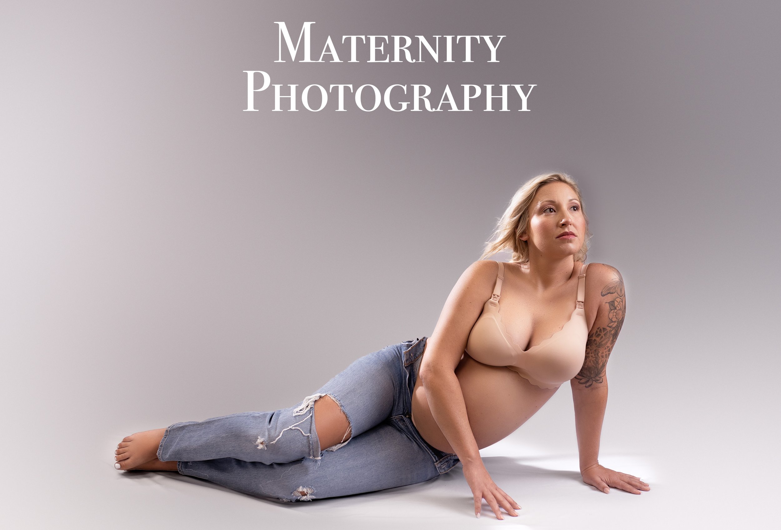 A pregnant woman with blonde hair lying on her side on a plain gray background, wearing ripped jeans and a beige bra, with a tattoo on her right arm, alongside the text 'Maternity Photography.Louisville Kentucky Newborn Photographer