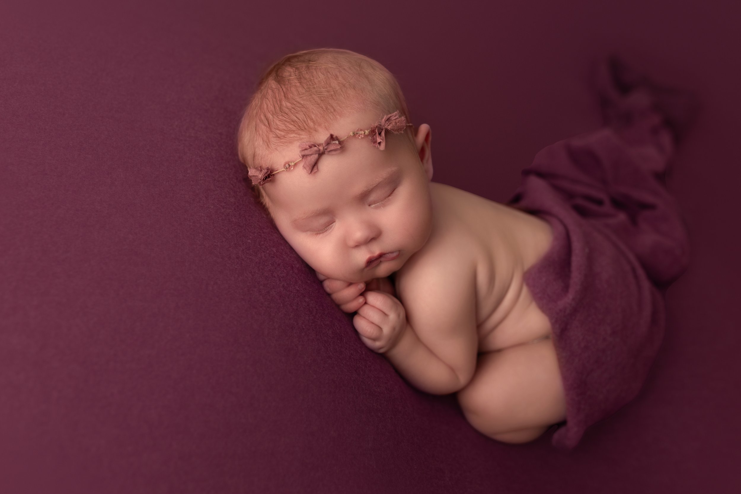 Newborn baby sleeping on purple blanket, wearing headband.