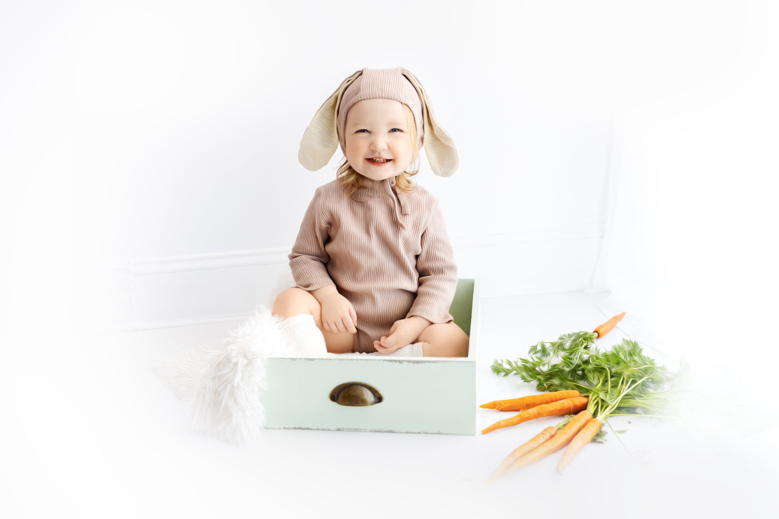 Toddler in bunny costume sitting in a drawer with carrots.
