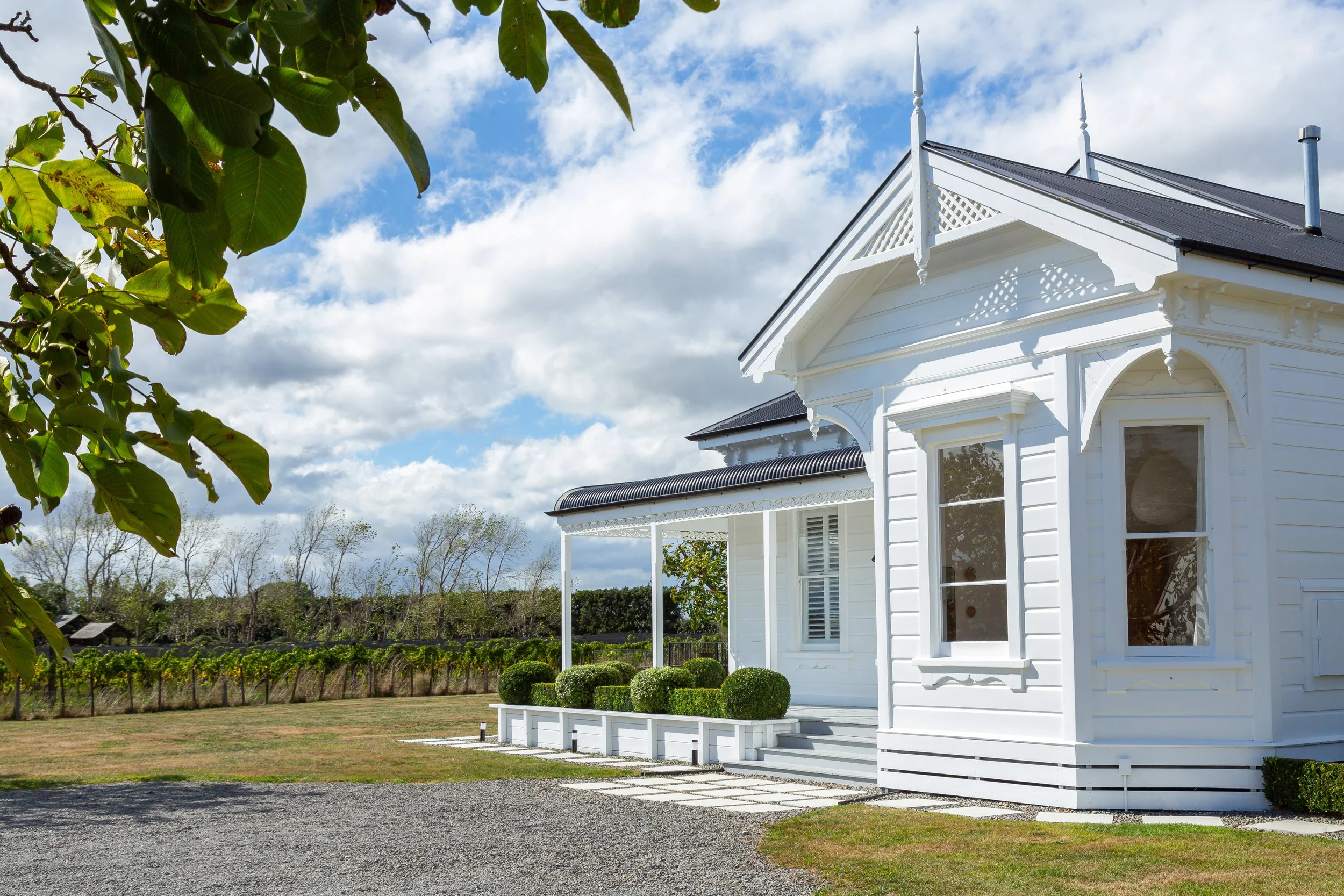 A large, charming white Victorian villa with intricate fretwork, a black front door and green topiary running along the porch. Great for weekend stays, small weddings, post wedding events, group gatherings, celebrations and holidays.