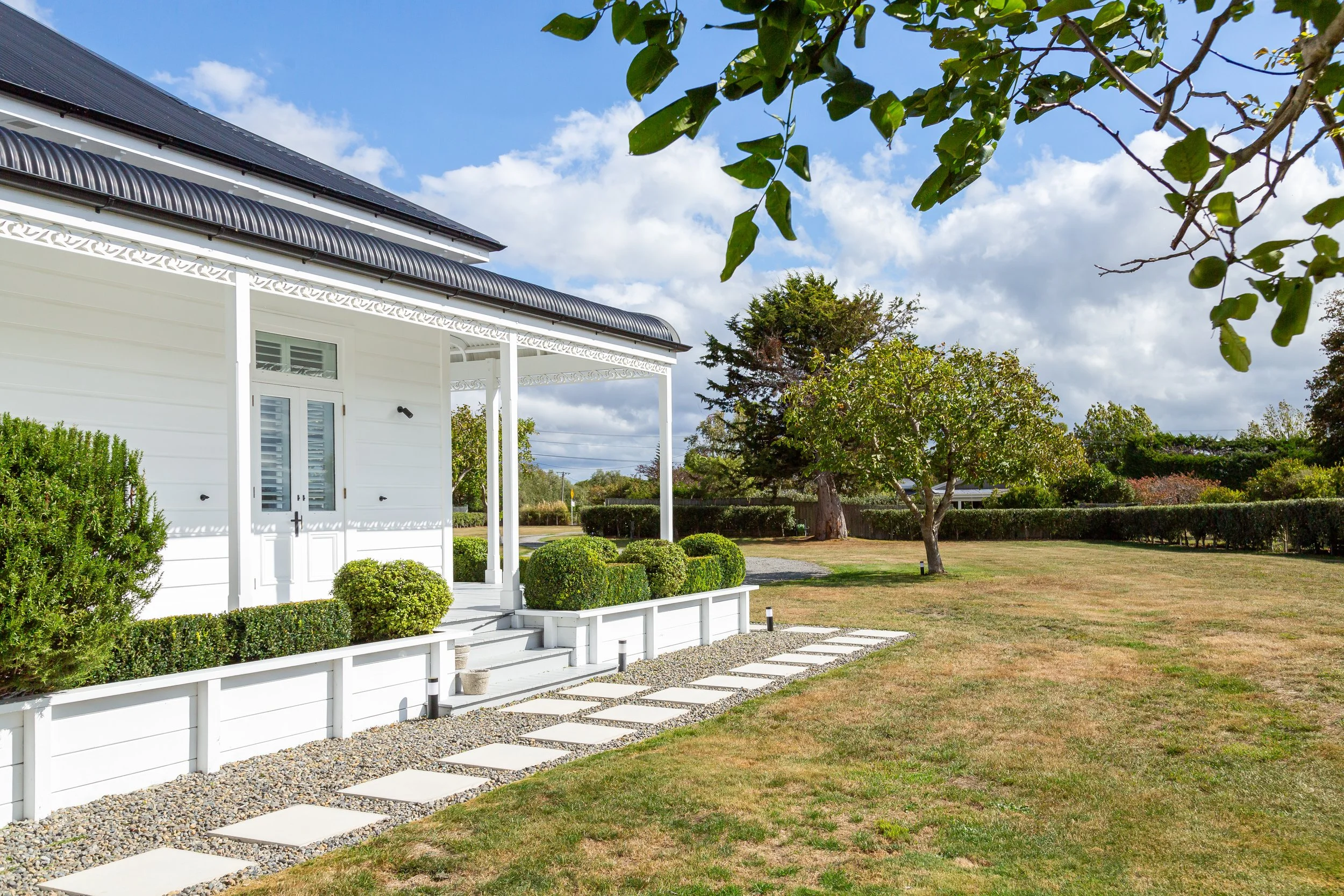 A large charming white Victorian villa surrounded by well-kept lawns, topiary and trees under a blue sky dotted with a few white clouds. Great for weekend stays, small weddings, post wedding events, group gatherings, celebrations and holidays.