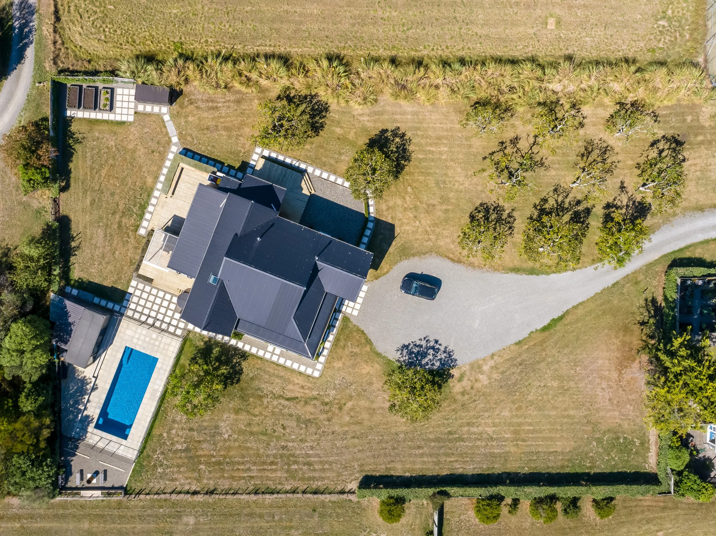 Aerial view of a large white villa and swimming pool set on a large country section with a driveway curving between large sprawling lawns and trees. Great for weekend stays, group gatherings, celebrations and holidays.