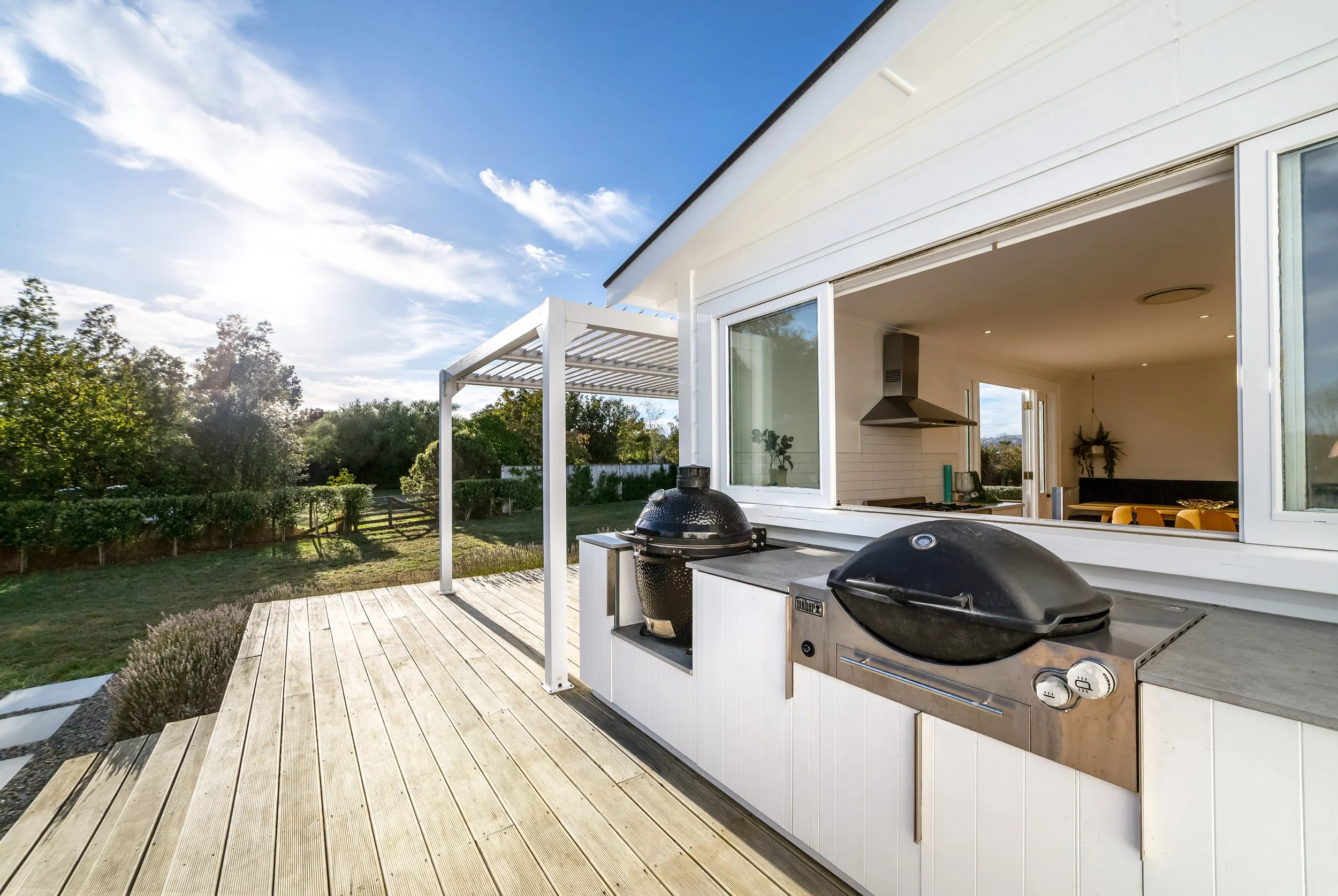 Large outdoor wooden deck with a built-in grill bbq area and view of a backyard with trees and well-kept lawns. Great for weekend stays, small weddings, post wedding events, group gatherings, celebrations and holidays.