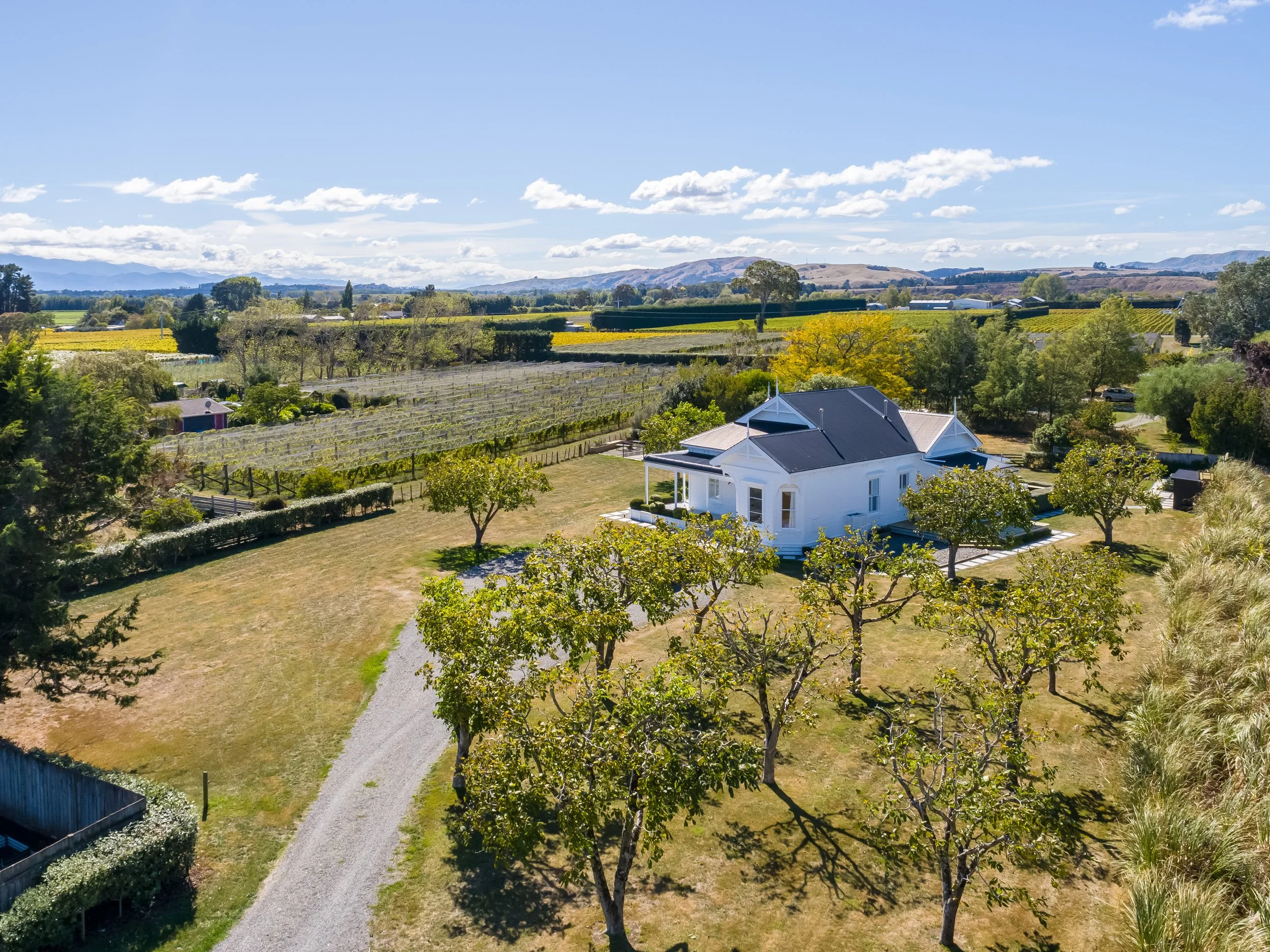Aerial view of a large white villa and swimming pool set on a large country section with a driveway curving between large sprawling lawns and trees. Great for weekend stays, group gatherings, celebrations and holidays.