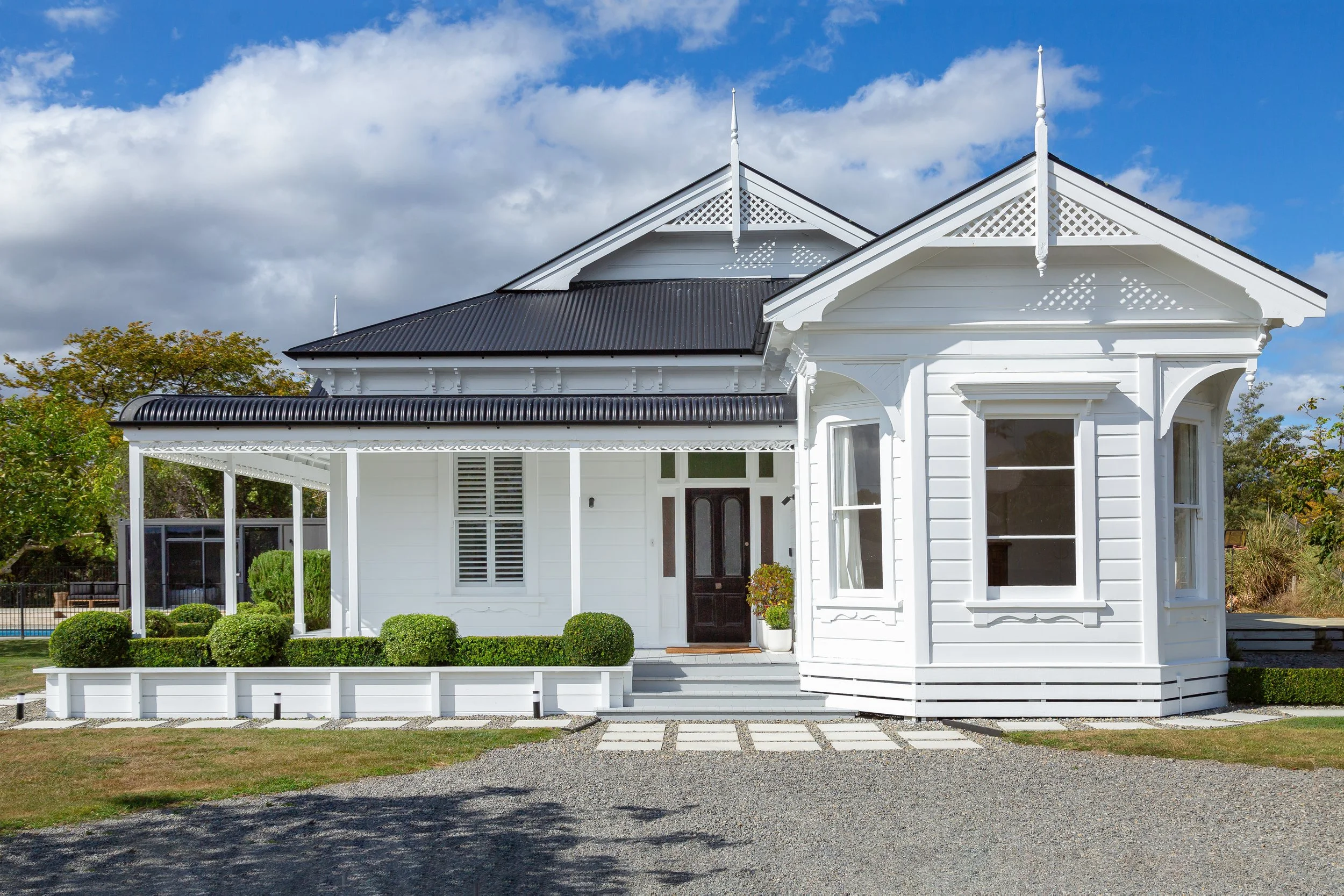 A large, charming white Victorian villa with intricate fretwork, a black front door and green topiary running along the porch. Great for weekend stays, small weddings, post wedding events, group gatherings, celebrations and holidays.