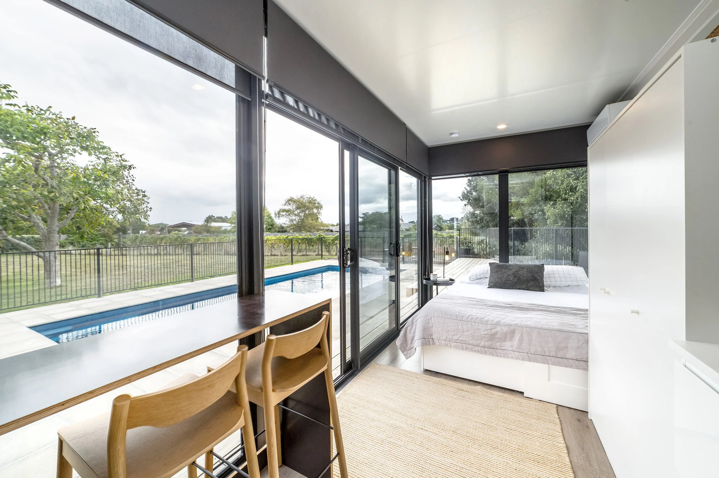 Interior view of the modern pool house living space with a queen size bed, panoramic window views to the pool and vineyards. Great for weekend stays, group gatherings, celebrations and holidays.