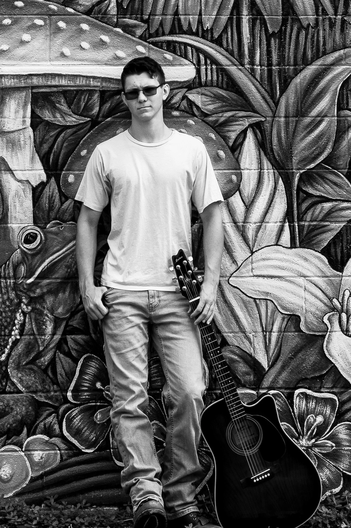 Lakeville student poses for senior portrait with his guitar in front of a mural in Frankenmuth, MI.