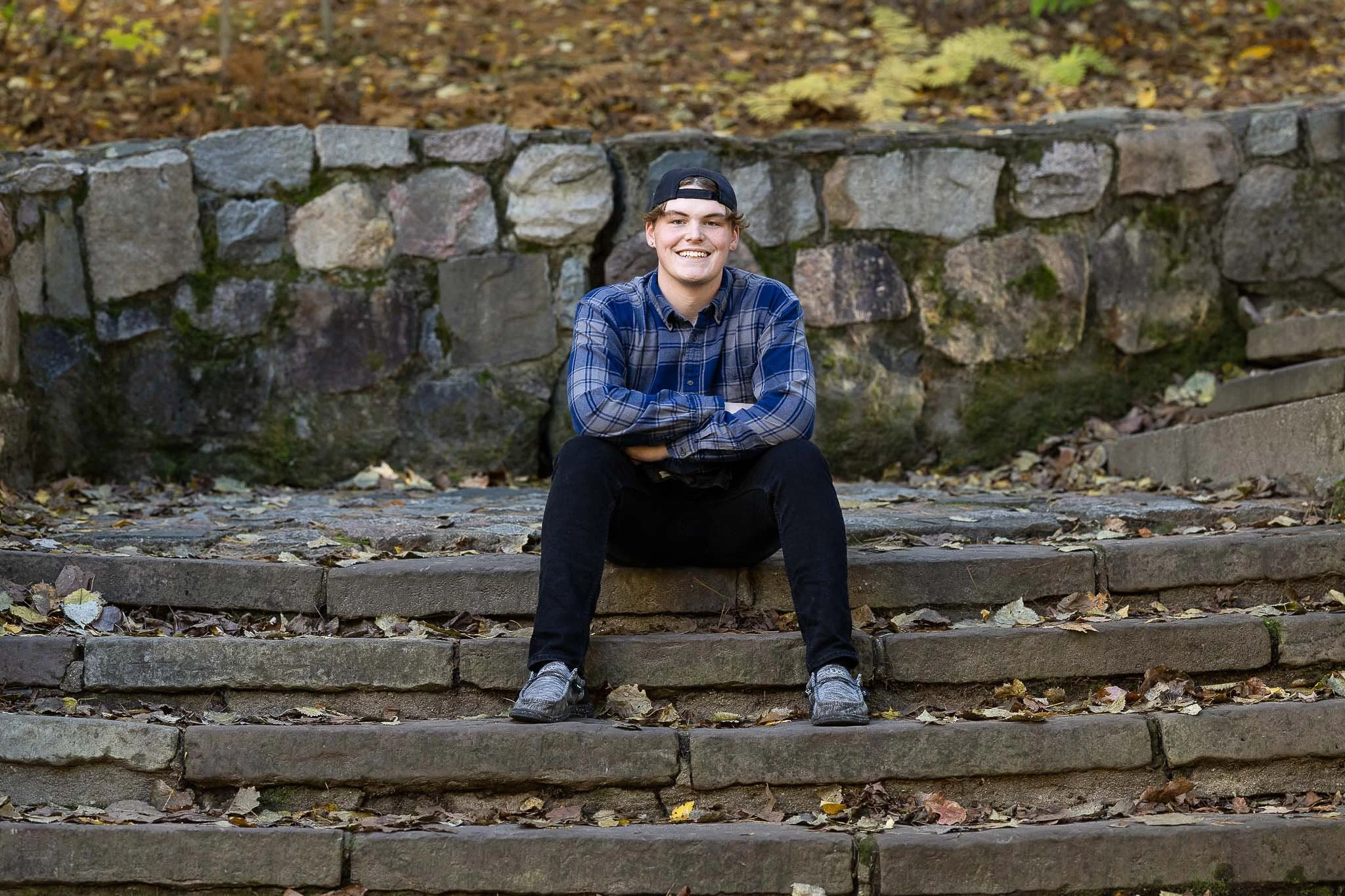 A young man smiles for his senior portrait session, sitting on stone steps at a park in Davison, MI.